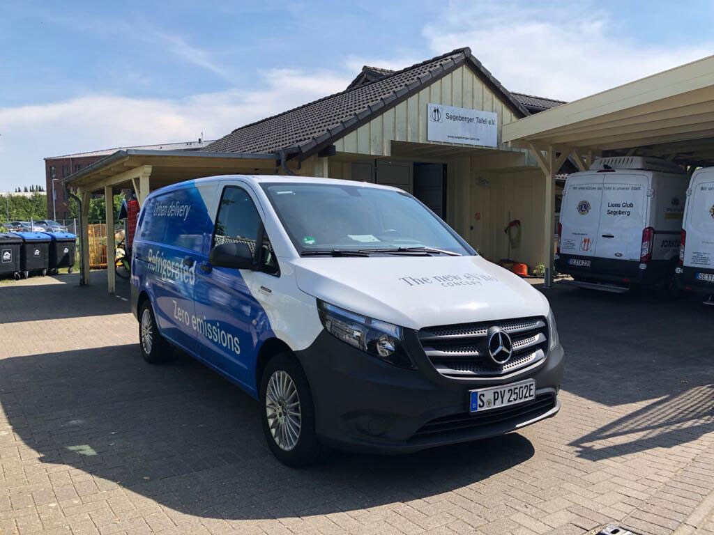 Ein Mercedes-Benz Van der Tafel Deutschland vor einem Haus und einer Garage.