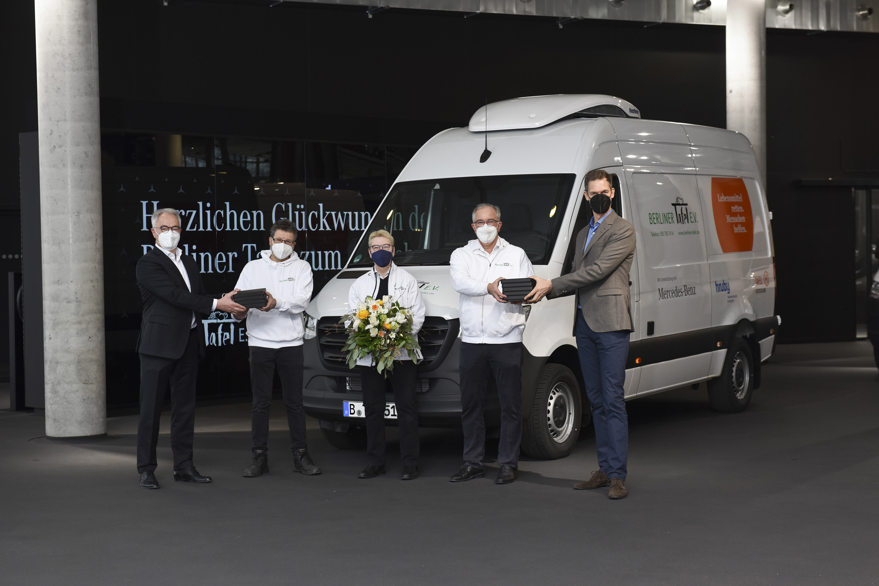 Mercedes-Benz | Tafel-Sponsoring Fünf Personen stehen vor einem Mercedes-Benz Sprinter feierlich zu einer offiziellen Übergabe. Eine Person hält einen Blumenstrauß in die Hände.