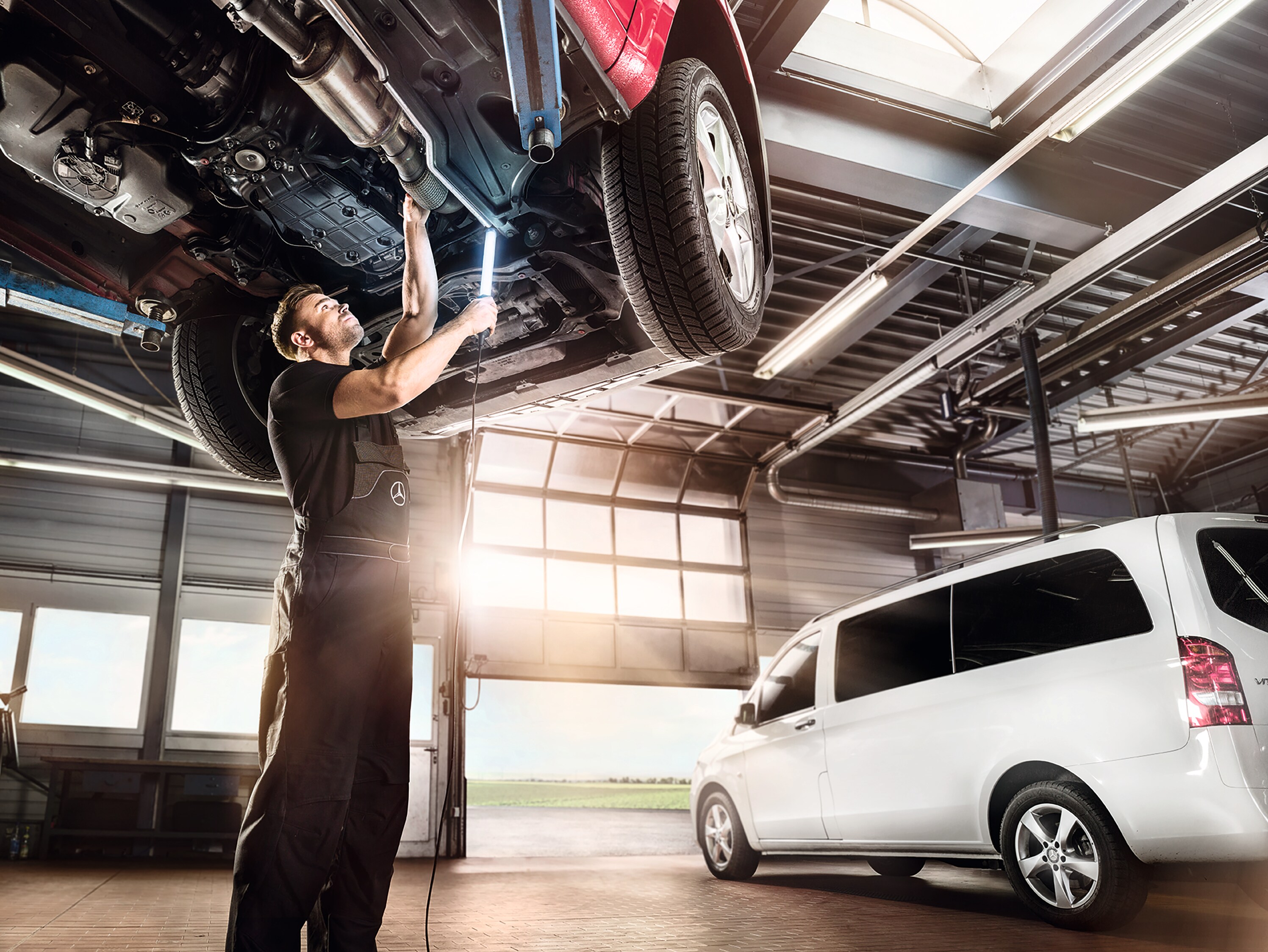 Ein Mercedes-Benz Transporter in einer Werkstatt. Ein Service Mitarbeiter schaut unter ein Fahrzeug.