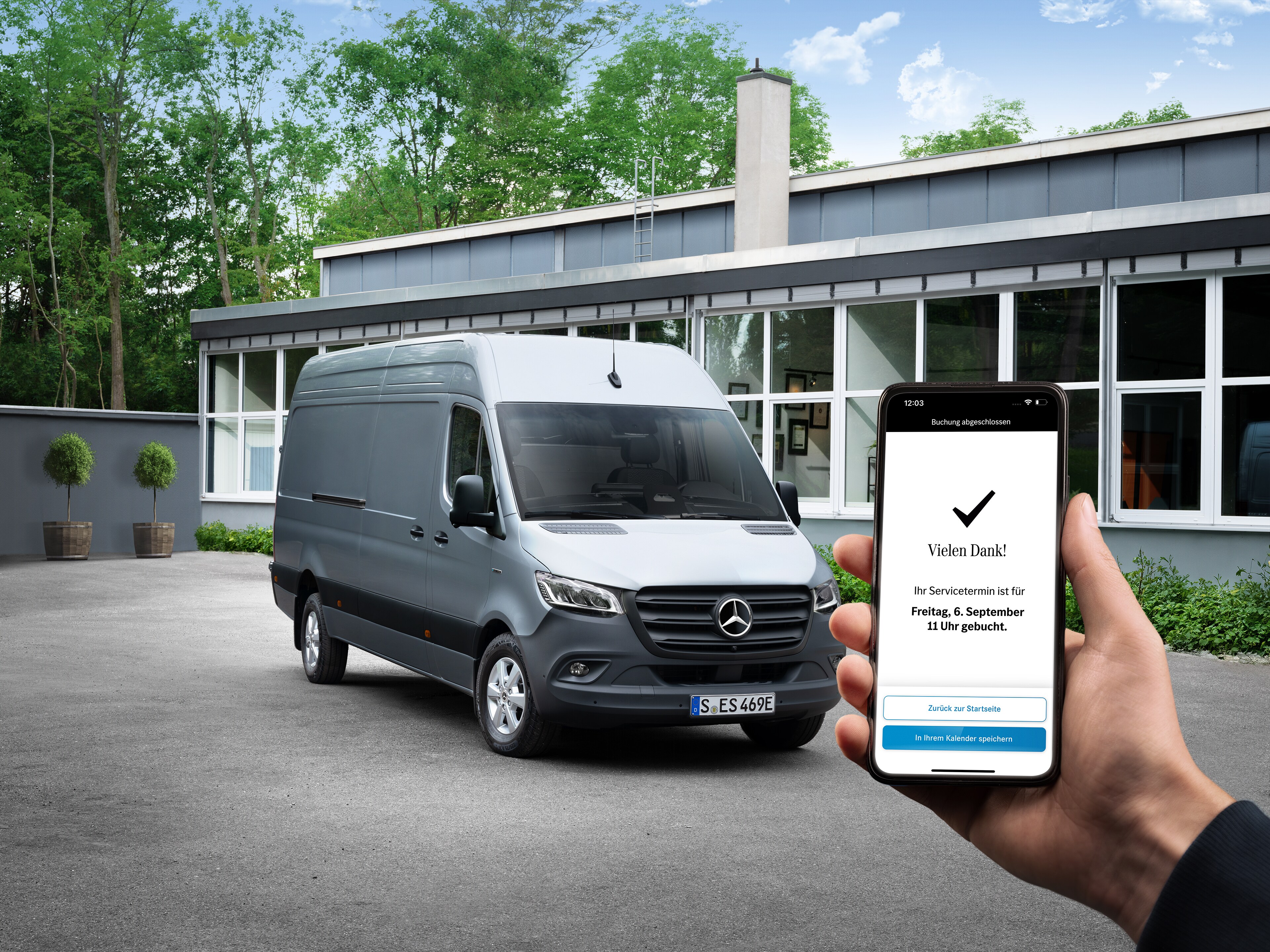 Eine Hand hält ein Smartphone vor einem Mercedes-Benz Transporter.