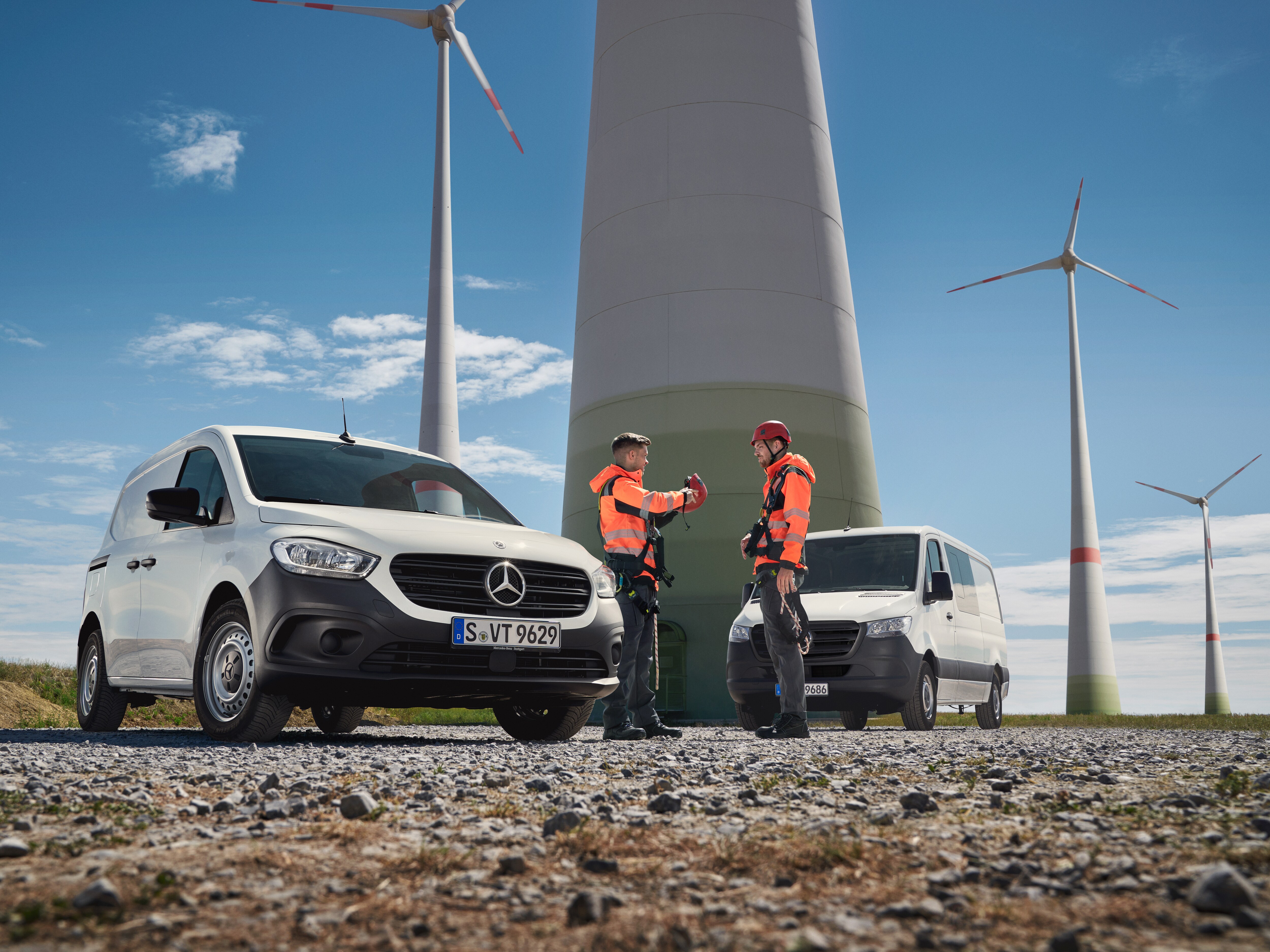 Zwei Mercedes-Benz Transporter vor einem Windradpark. Zwei Personen in Arbeitskleidung sprechen.