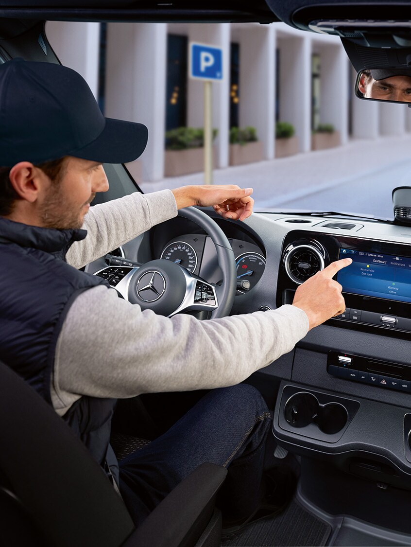 Fahrer bedient im Auto die Mercedes-Benz Service App auf dem Display, um Fahrzeugdaten und Serviceoptionen zu prüfen.