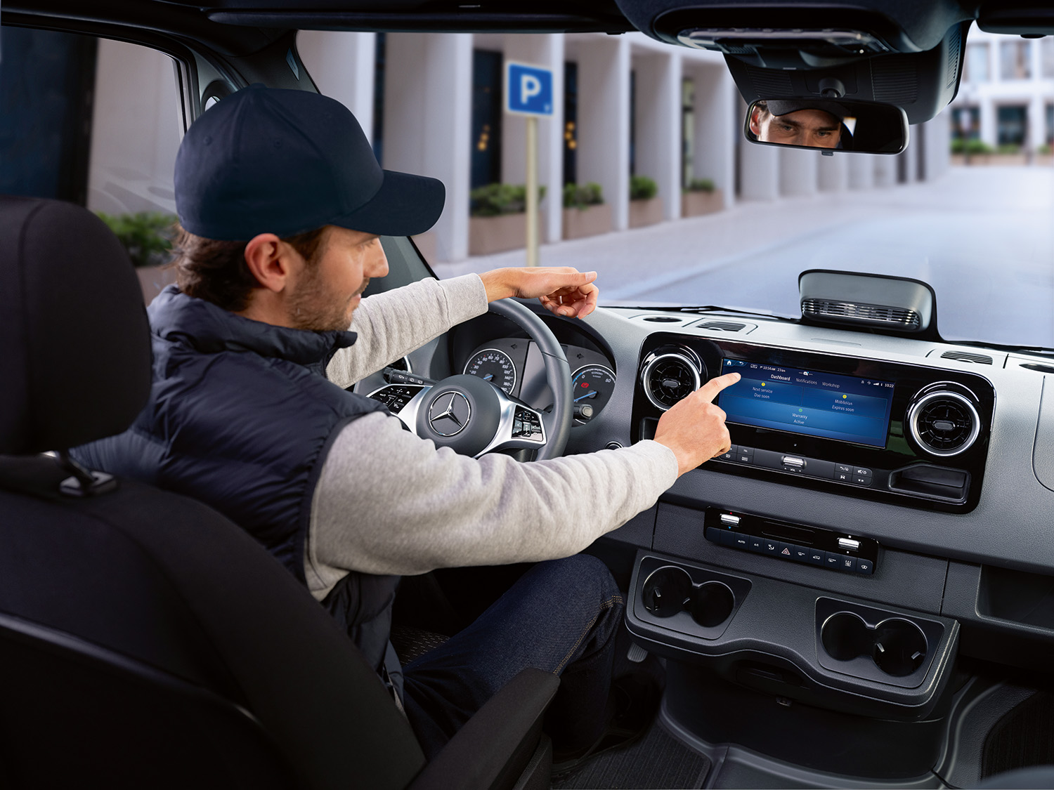 Onboard Service App | Mercedes-Benz Transporter. Fahrer bedient im Auto die Mercedes-Benz Service App auf dem Display, um Fahrzeugdaten und Serviceoptionen zu prüfen.