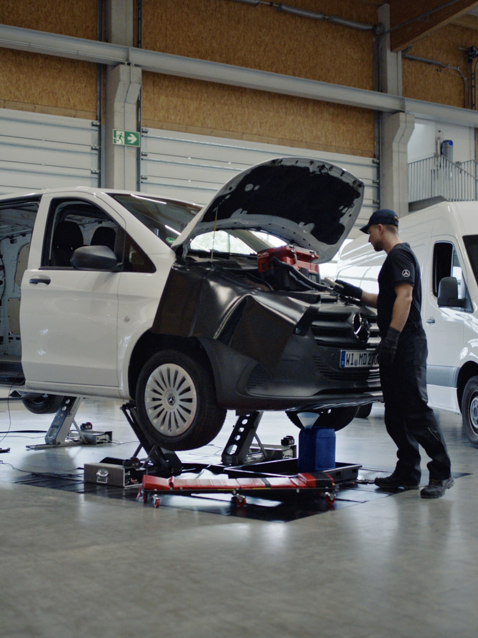 Ein Techniker repariert auf einem Rollbrett liegend einen weißen Mercedes-Benz Vito.