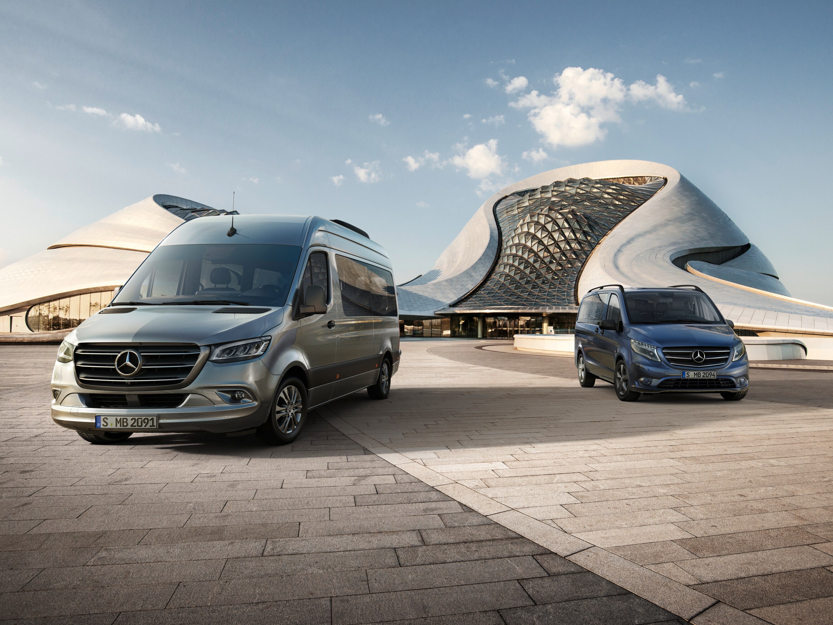 Zwei Mercedes-Benz Transporter vor modernen geschwungenen Gebäudesillouetten.