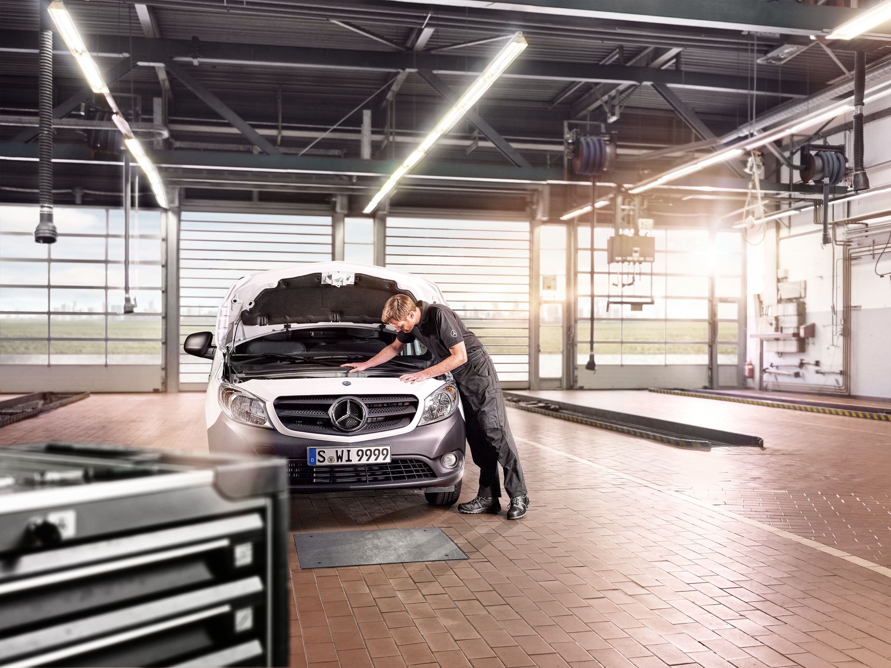 Ein Mercedes-Benz Service Mitarbeiter prüft bei geöffneter Motorhaube einen Transporter in einer Werkstatt.