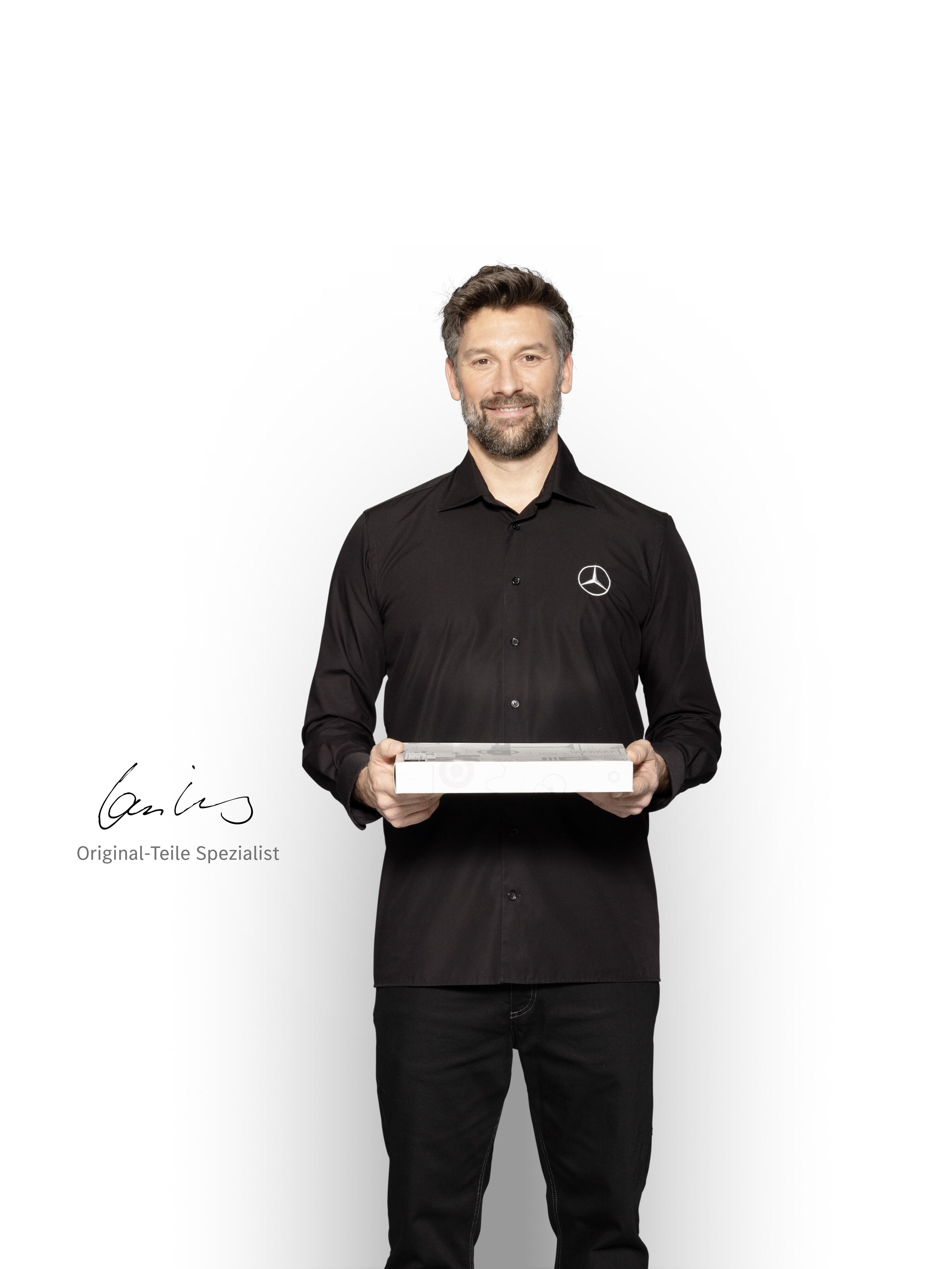 Mercedes-Benz Techniker mit einer Box in der Hand, um Mercedes-Benz Original-Teile zu zeigen.