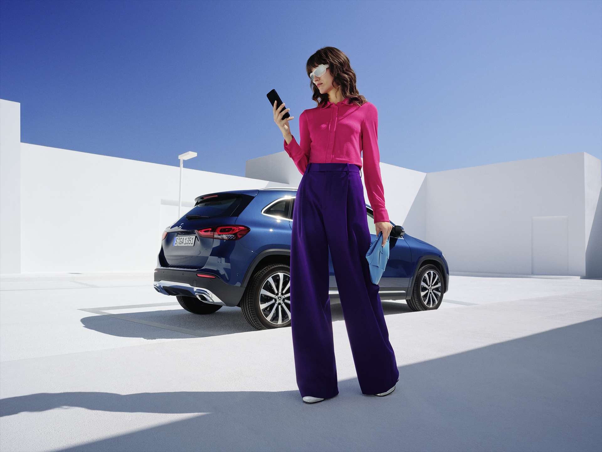 Digitale Extras | Mehr erfahren | Mercedes-Benz Eine Frau steht vor dem Mercedes-Benz GLA und schaut auf ihr Telefon.