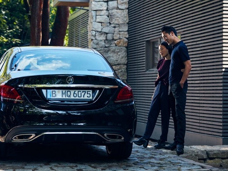 Eine Frau und ein Mann stehen neben einem schwarzen Mercedes-Benz.