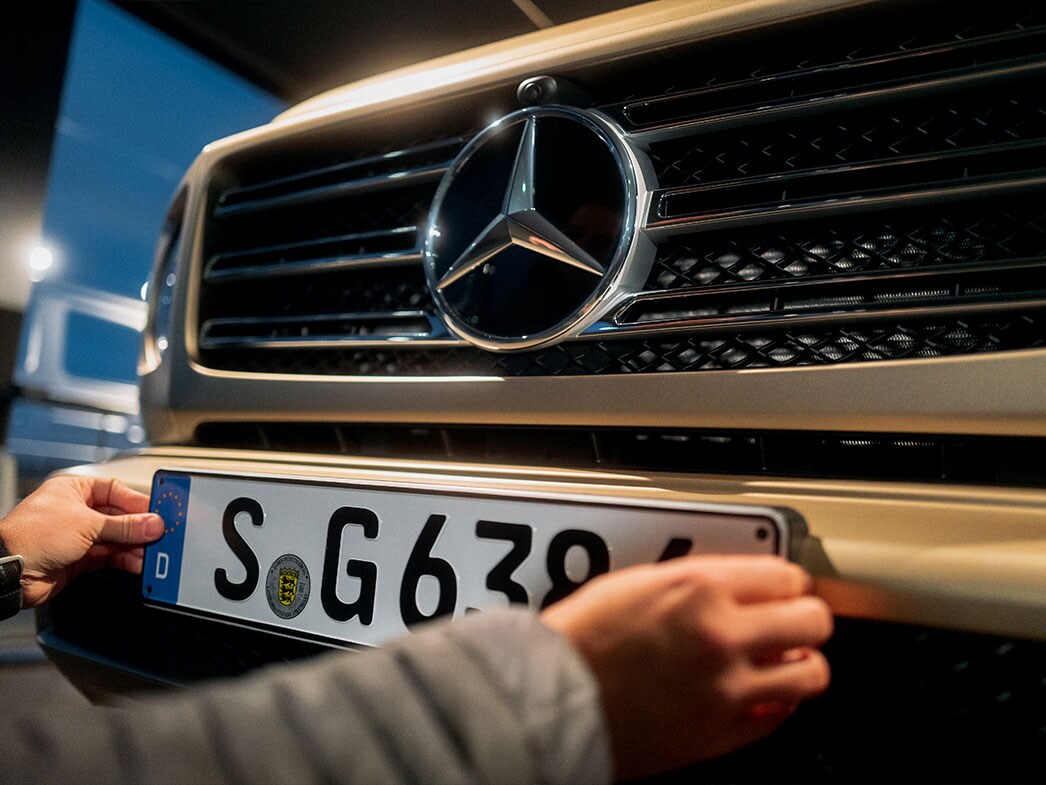 Ein Nummernschild wird an eine goldene Mercedes-Benz G-Klasse angebracht.