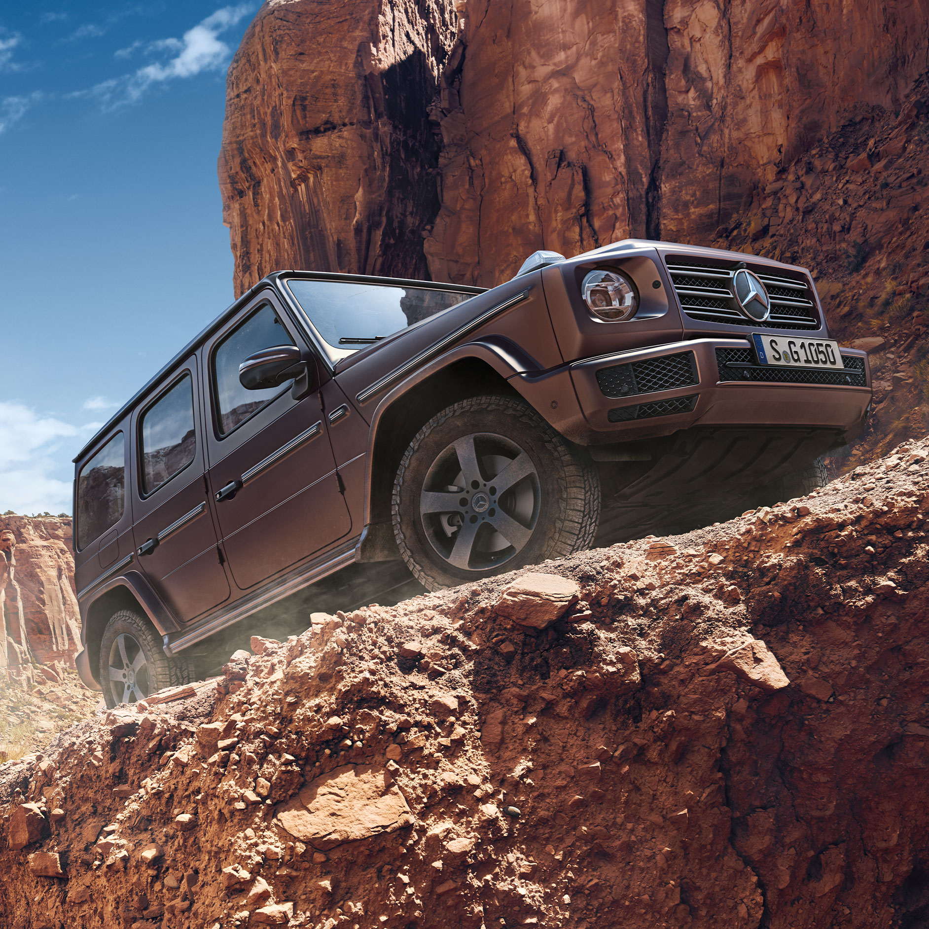 Werksabholung am G-Class Experience Center | Mercedes-Benz Seitenansicht der Mercedes-Benz G-Klasse in den Bergen einen steinigen Weg hochfahrend.