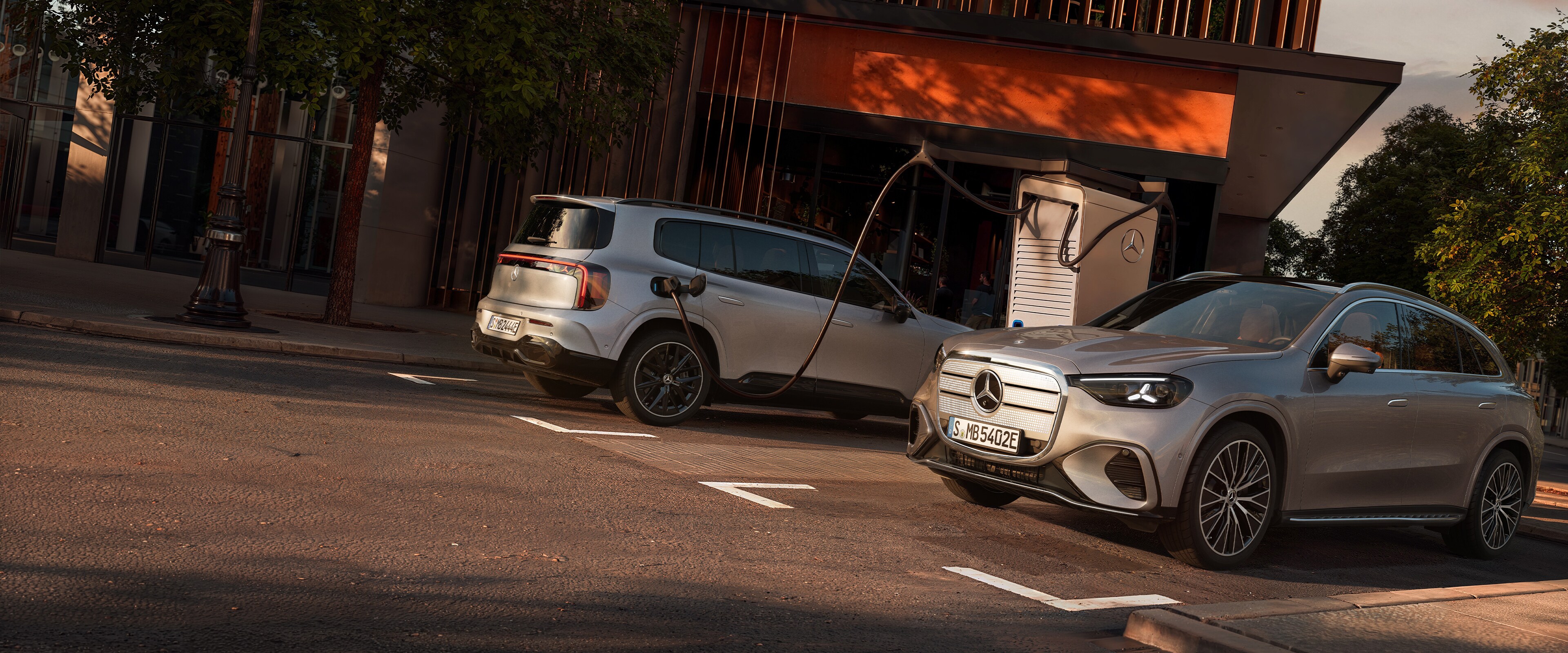 Zwei Elektrofahrzeuge von Mercedes-Benz stehen auf einem Parkplatz und werden geladen.