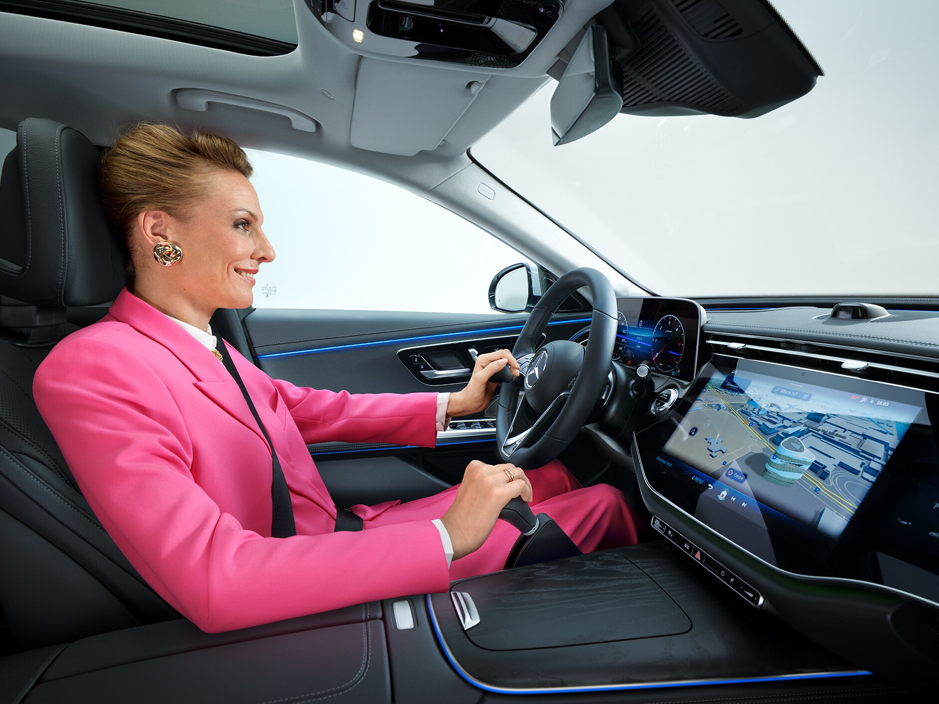 Innenansicht einer zu einem barrierefreien Auto umgebauten Mercedes-Benz E-Klasse, mit einer Frau am Lenkrad, die einen Lenkradknauf und ein Handbediengerät benutzt.