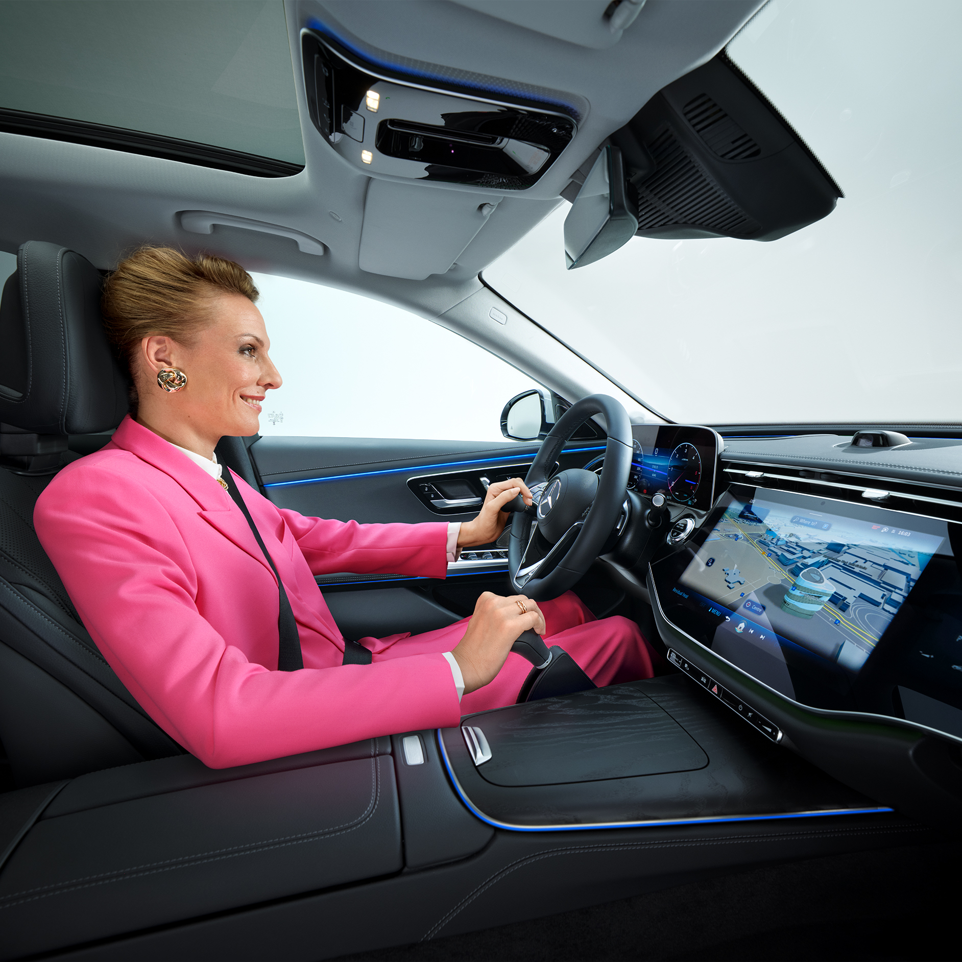 "More Mobility"-Ratgeber | Fahrhilfen | Mercedes-Benz Innenansicht einer zu einem barrierefreien Auto umgebauten Mercedes-Benz E-Klasse, mit einer Frau am Lenkrad, die einen Lenkradknauf und ein Handbediengerät benutzt.