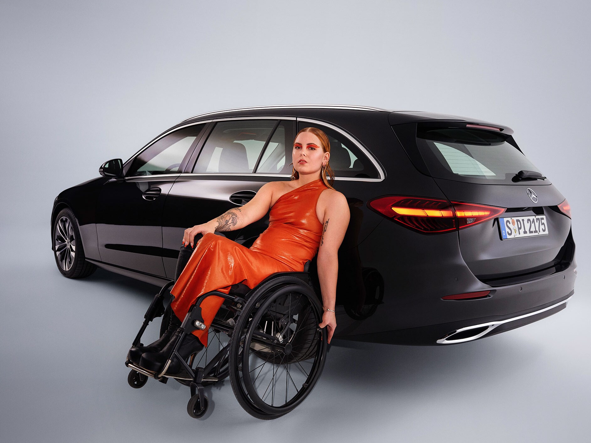 Ein behindertengerechtes Auto - das C-Klasse T-Modell in einer schrägen Heckansicht und eine Frau im Rollstuhl.