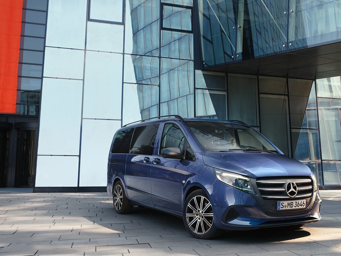 Ein blauer Mercedes‑Benz Vito Tourer mit Schiebetür vor einem modernen Gebäude.