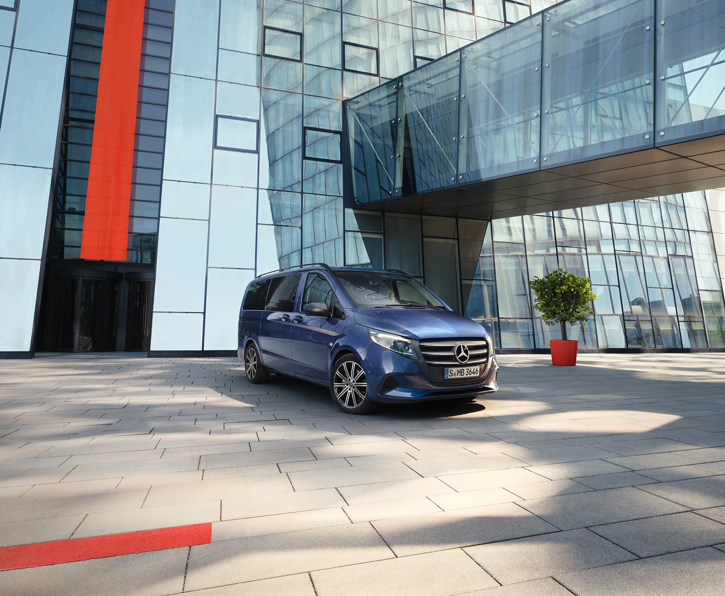 Van- und Camper-Modelle | Mercedes-Benz Vans. Ein blauer Mercedes‑Benz Vito Tourer mit Schiebetür vor einem modernen Gebäude.