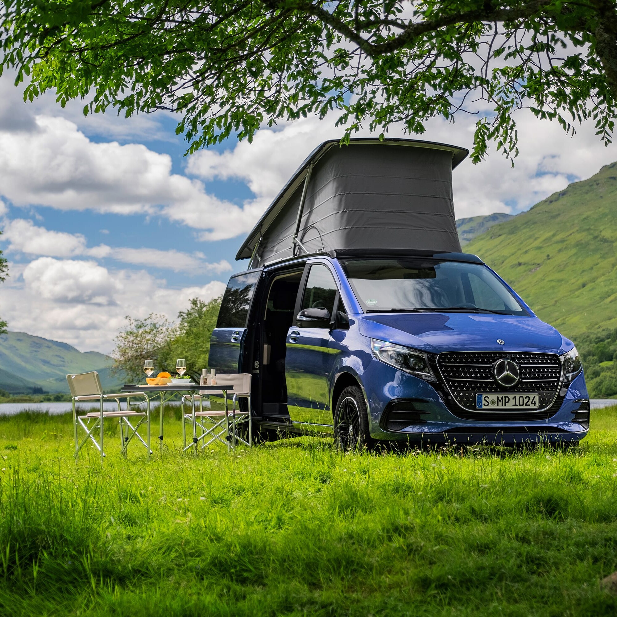 Ein dunkelblauer Marco Polo steht auf einer grünen Wiese  vor malerischer Landschaft.