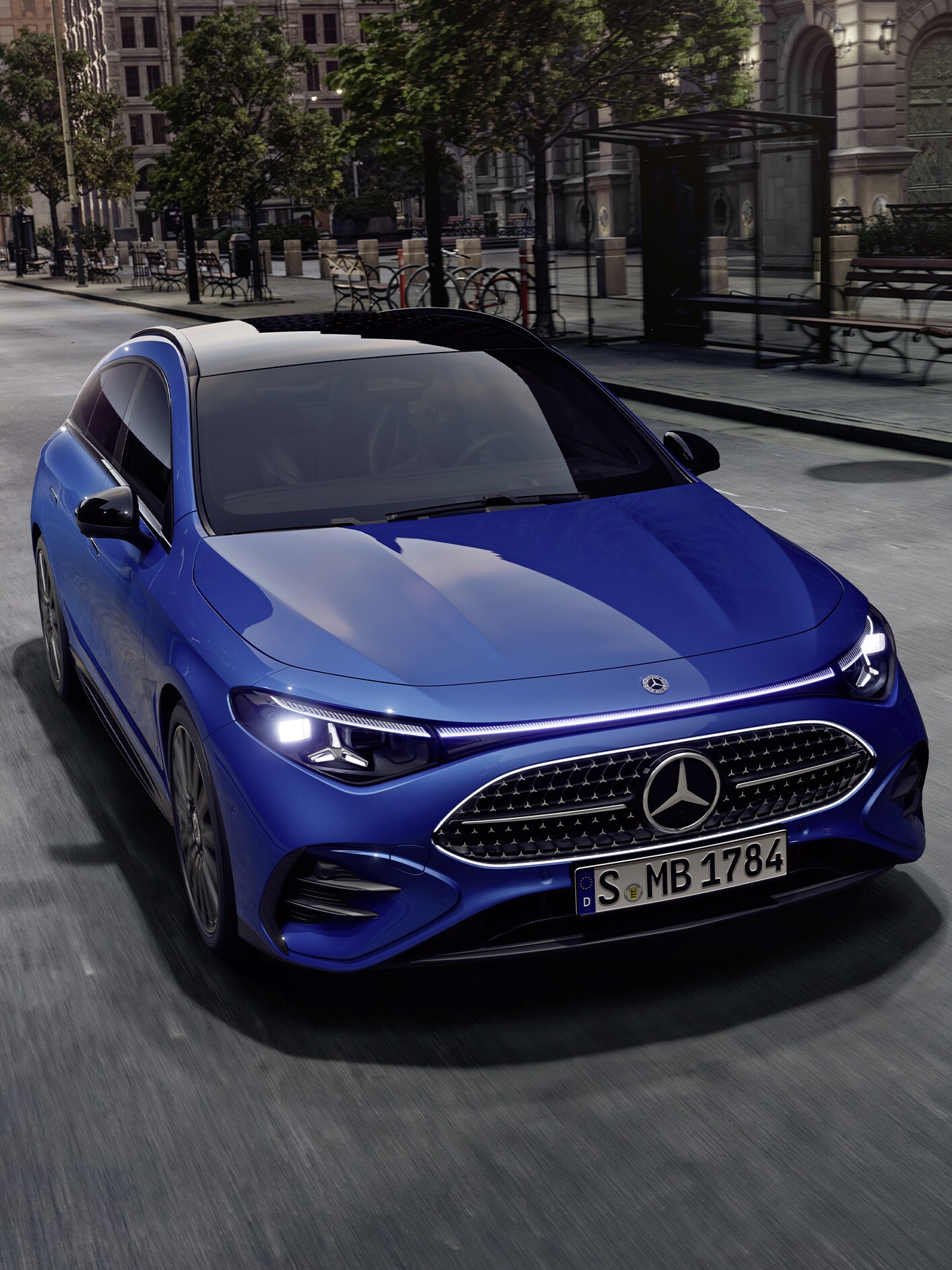 Ein strahlend blauer CLA Shooting Brake mit leuchtenden Scheinwerfern auf einer grauen Straße.