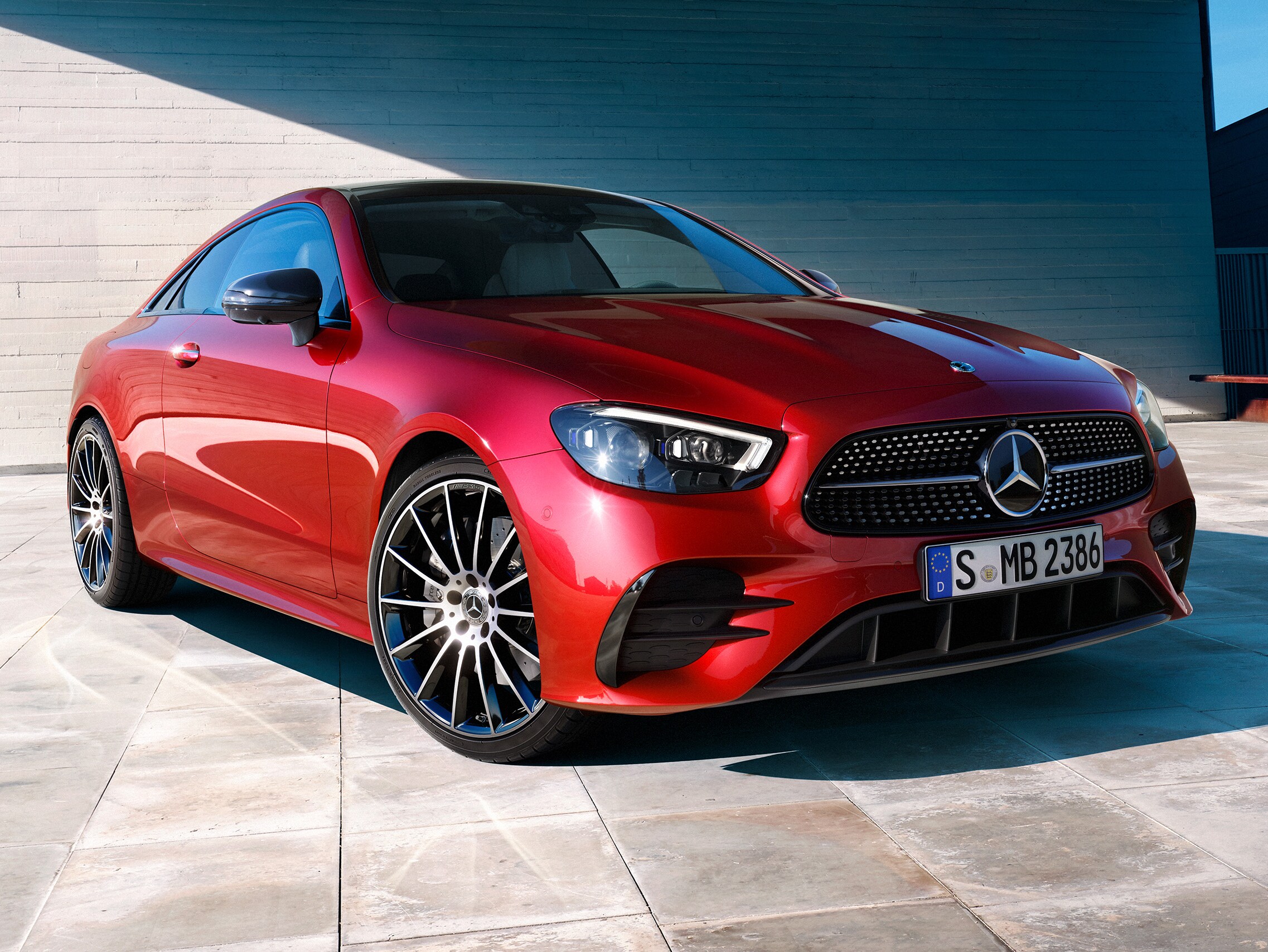 Ein rotes E-Klasse Coupé vor einem beigen Gebäude.
