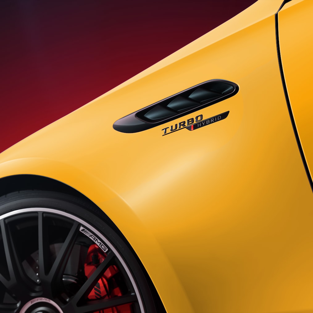 Nahaufnahme eines gelben Mercedes-AMG mit „Turbo Hybrid“-Schriftzug am Kotflügel und sichtbarem Teil des schwarzen Leichtmetallrads.