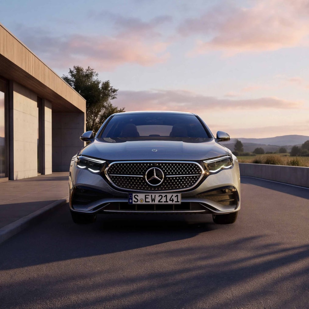 Eine Frontansicht einer parkenden E-Klasse Limousine von Mercedes-Benz bei Abenddämmerung neben einem Haus.