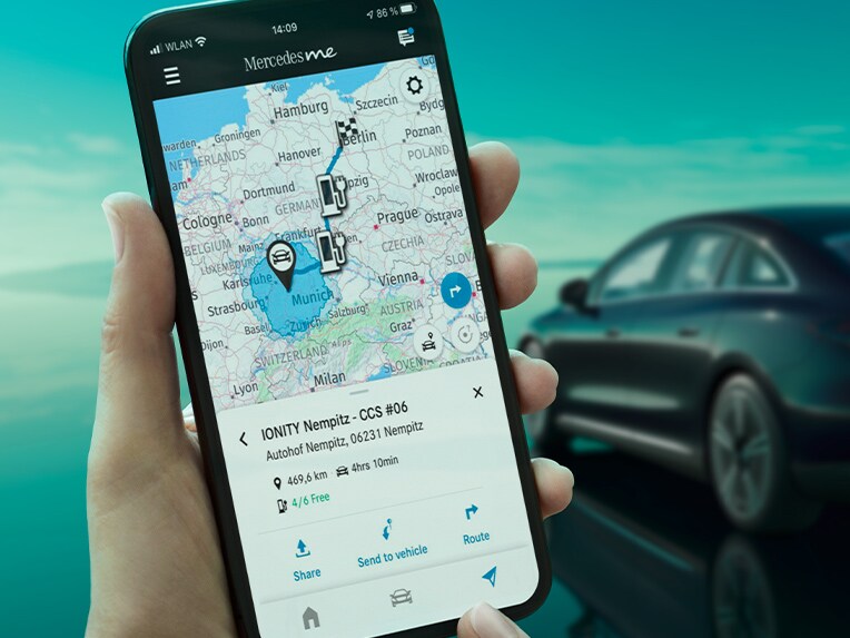 Die Mercedes-Benz ECO Coach App auf einem Smartphone, im Hintergrund die EQE Limousine, die an einer Wallbox lädt.