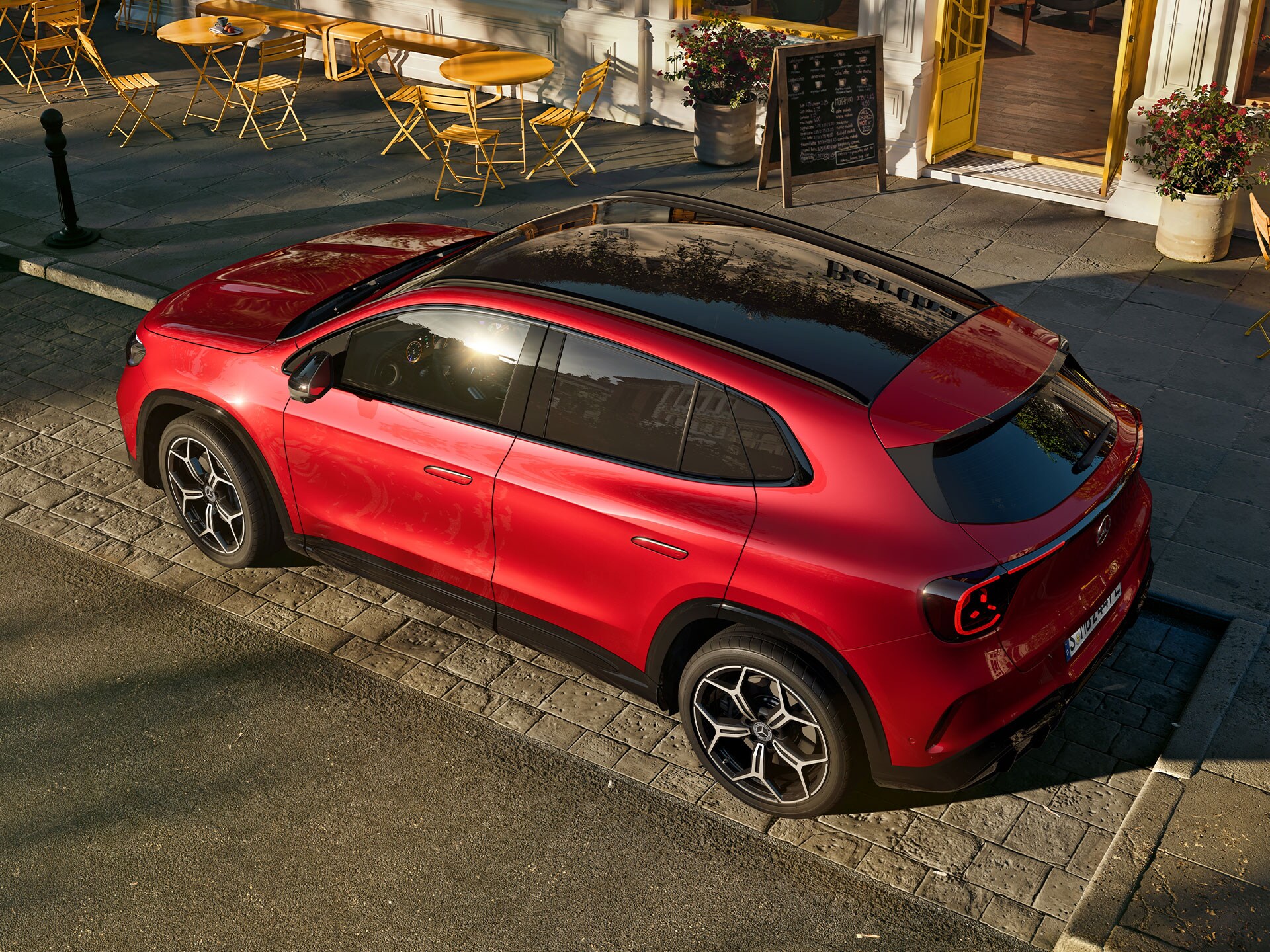 Der neue elektrische GLA in Rot in seitlicher Frontalansicht steht vor einem Cafe