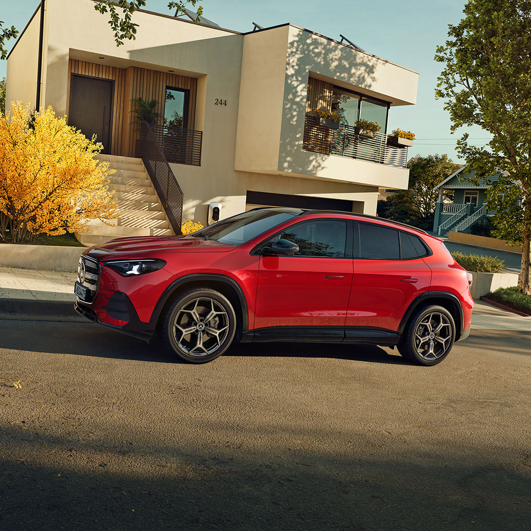 Angebote | Mercedes-Benz Der neue elektrische GLA in Rot in seitlicher Frontalansicht steht auf einer Straße in einer Wohnsiedlung.