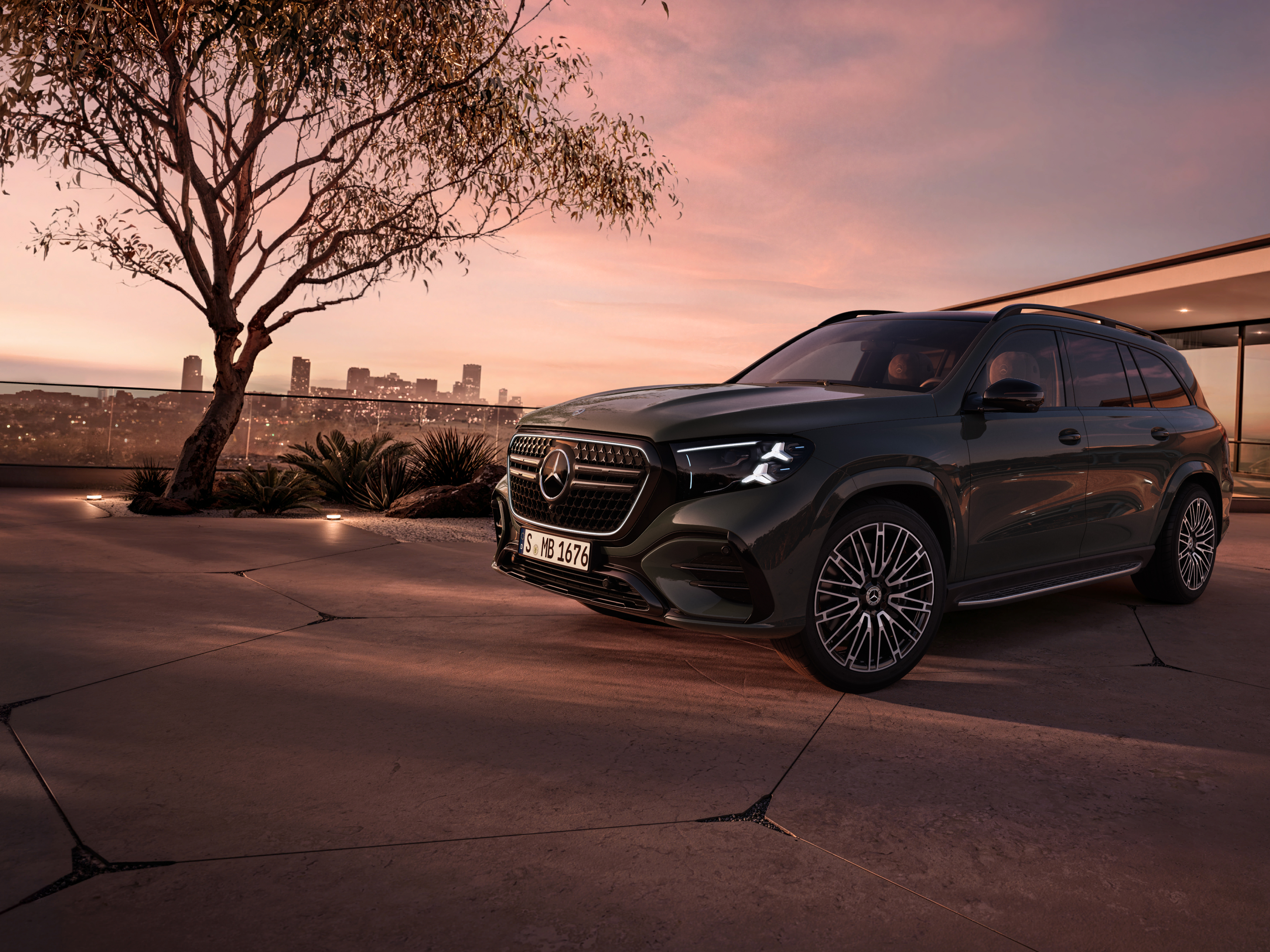 Dier neue Mercedes-Benz GLS, in seitlicher Frontansicht parkend vor einem Haus bei Sonnenuntergang.