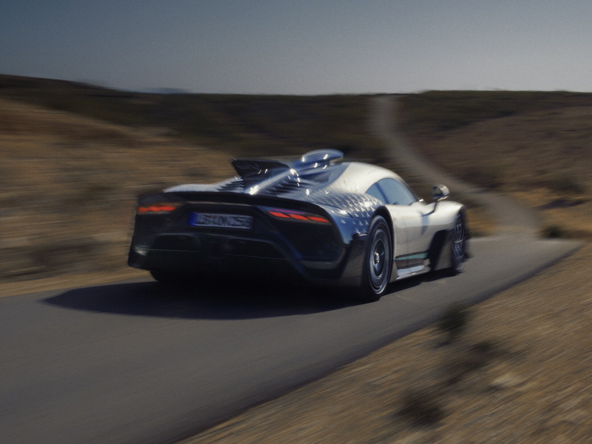 Ein Mercedes-AMG ONE Hypercar in Fahrt auf einer gewundenen Landstraße, von hinten links aufgenommen.