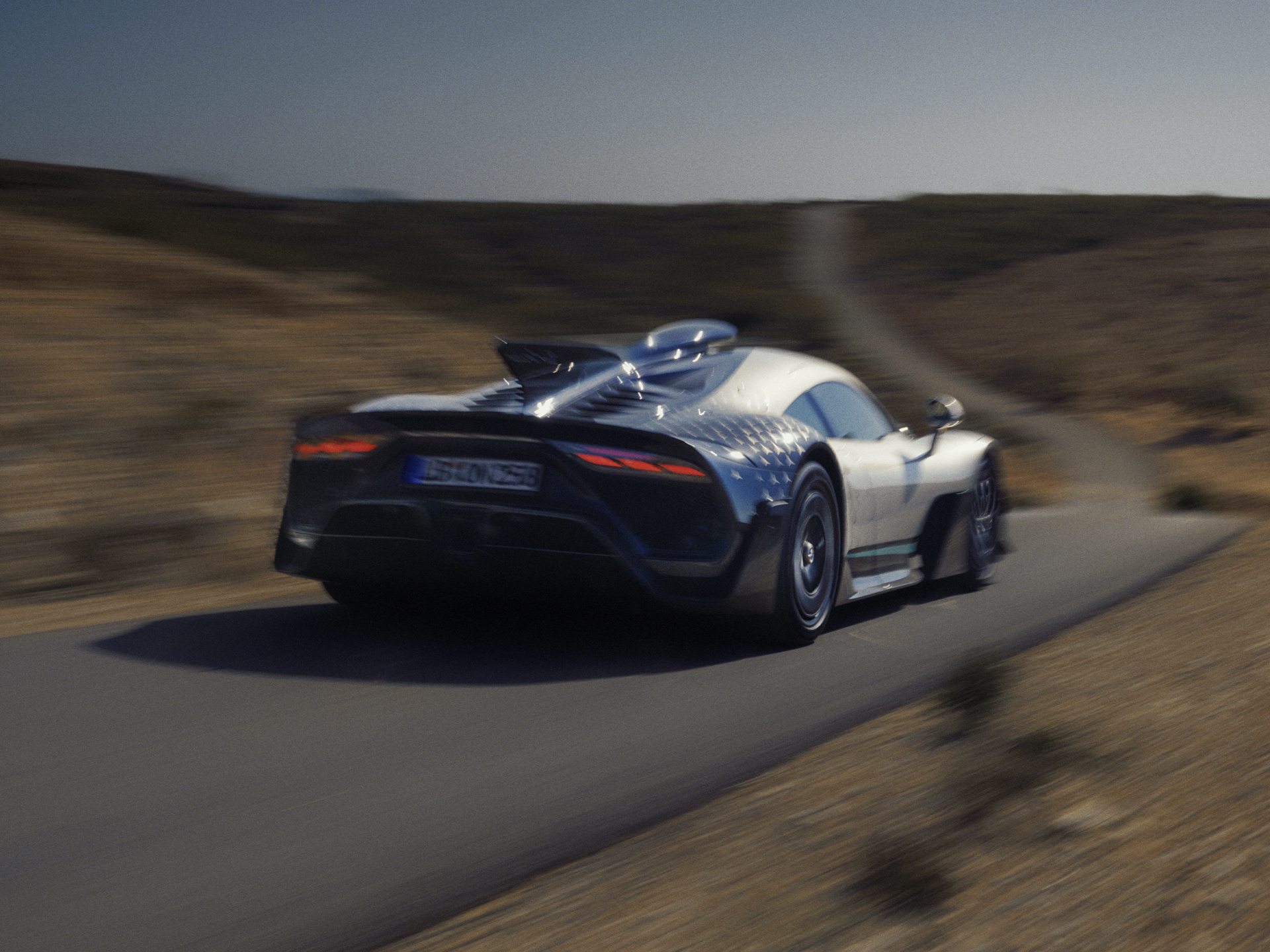 Normen brechen | Die Marke | Mercedes-AMG Ein Mercedes-AMG ONE Hypercar in Fahrt auf einer gewundenen Landstraße, von hinten links aufgenommen.