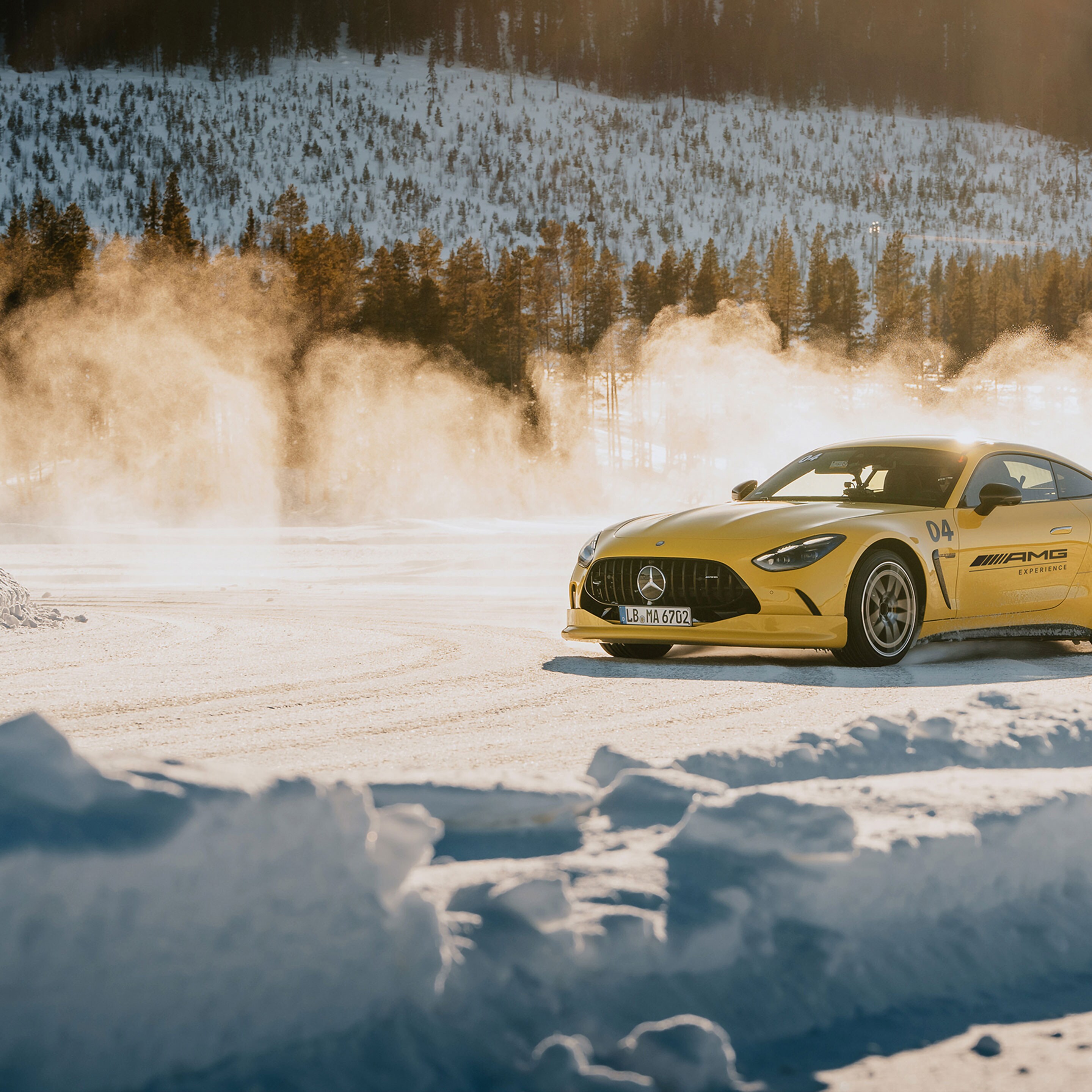 Ein gelber Mercedes-AMG GT Sportwagen driftet dynamisch über eine verschneite Piste im Gegenlicht.