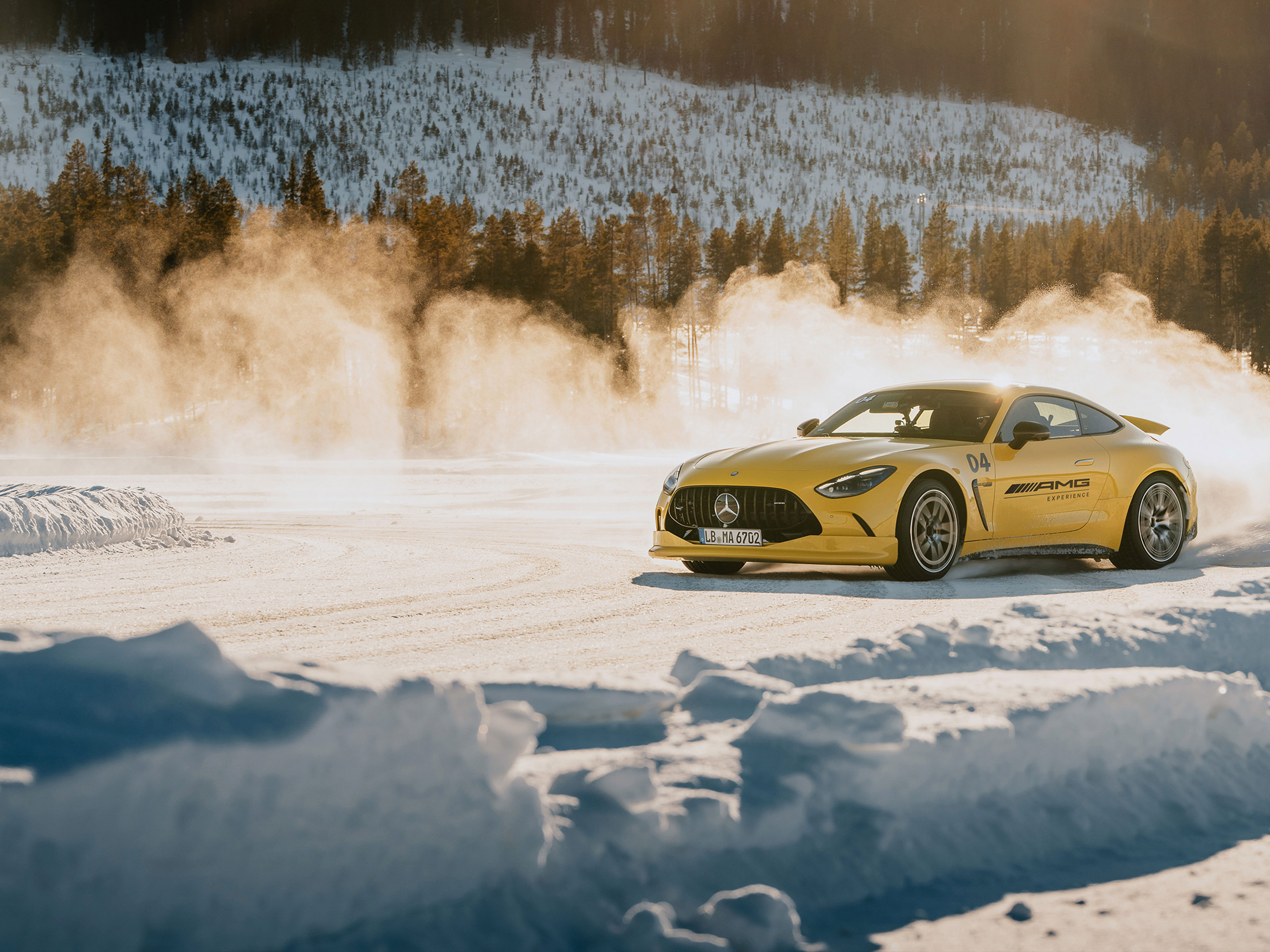 AMG Experience | Mercedes-AMG Ein gelber Mercedes-AMG GT Sportwagen driftet dynamisch über eine verschneite Piste im Gegenlicht.