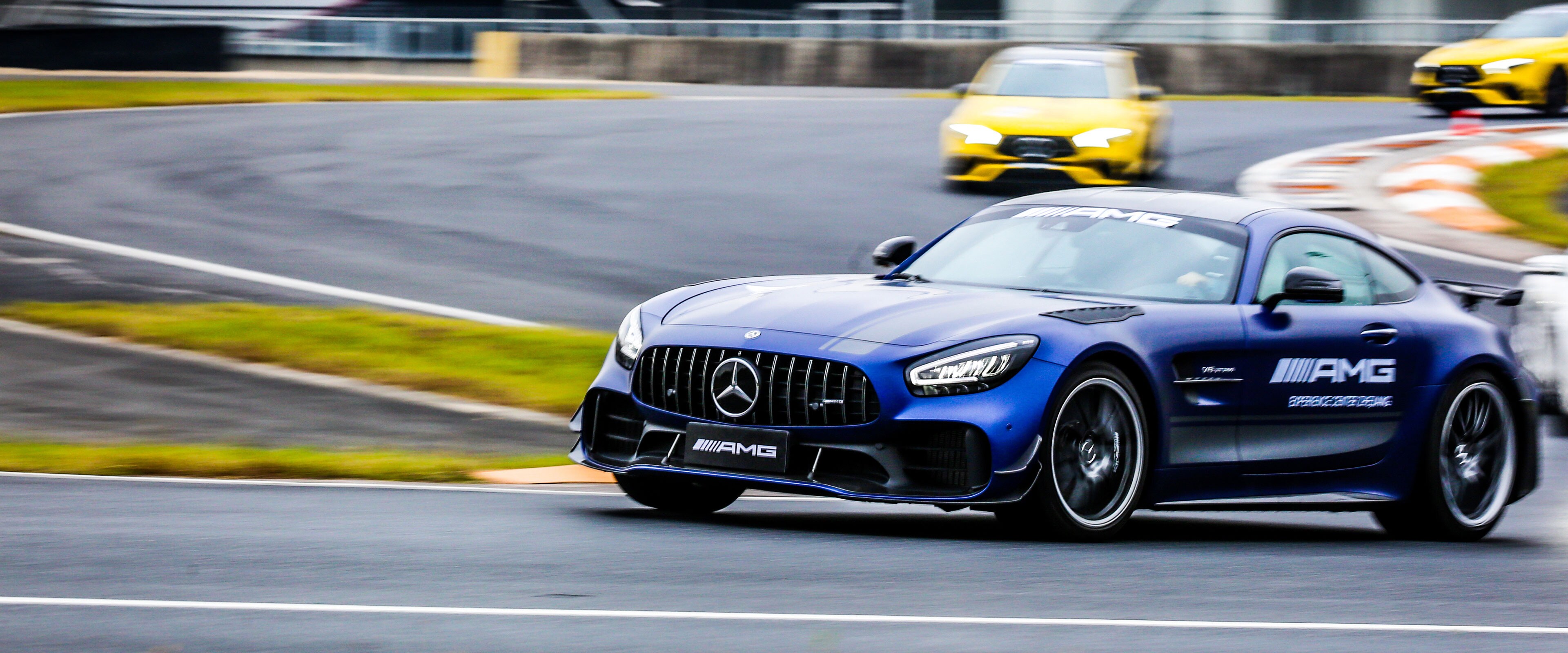 Ein dunkelblauer Mercedes-AMG GT R fährt auf einer Rennstrecke und wird von zwei weiteren Autos verfolgt.
