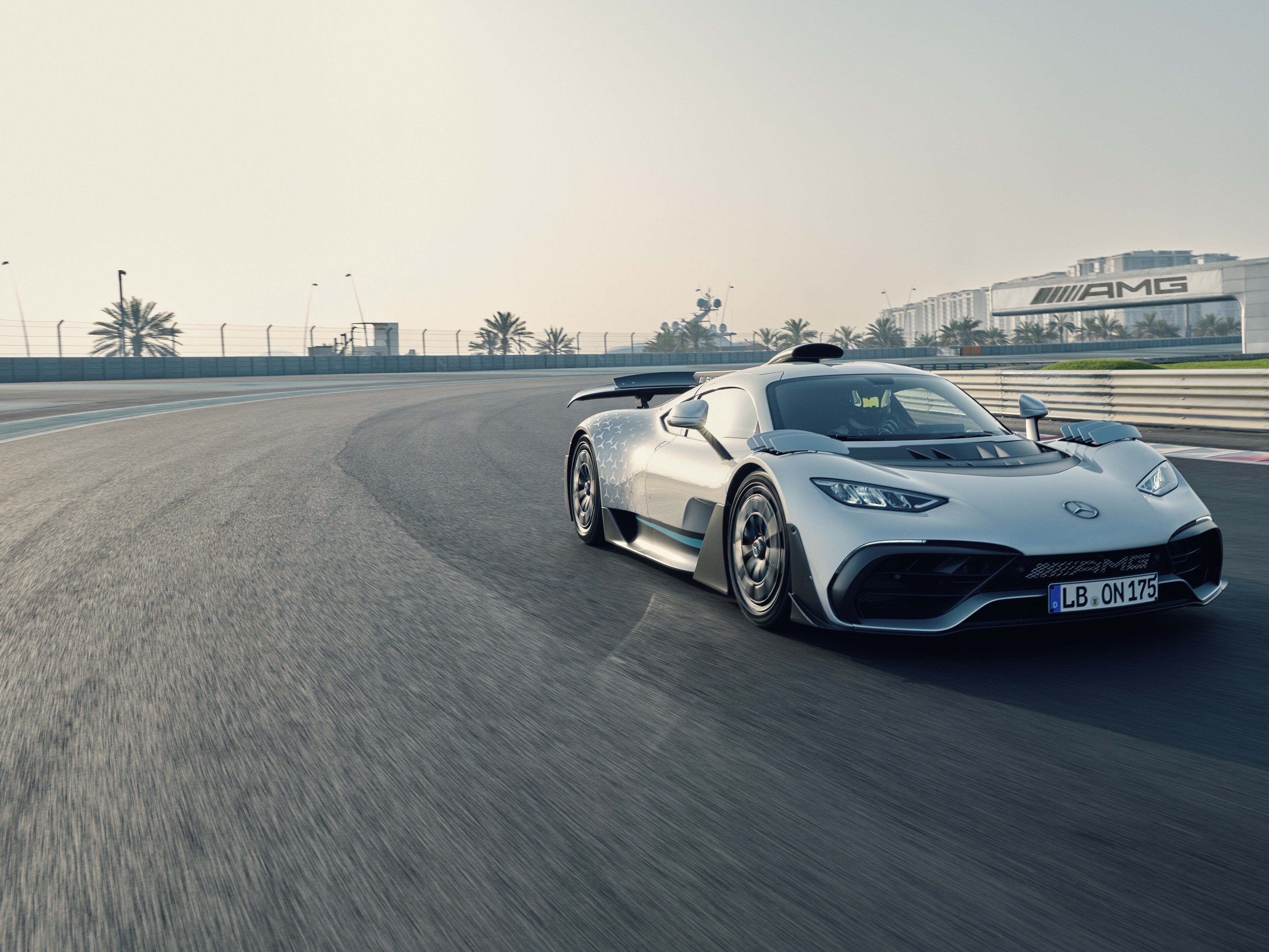Der Mercedes-AMG ONE rast über eine Rennstrecke. Auf einer Brücke im Hintergrund ist ein großes AMG-Logo zu sehen.