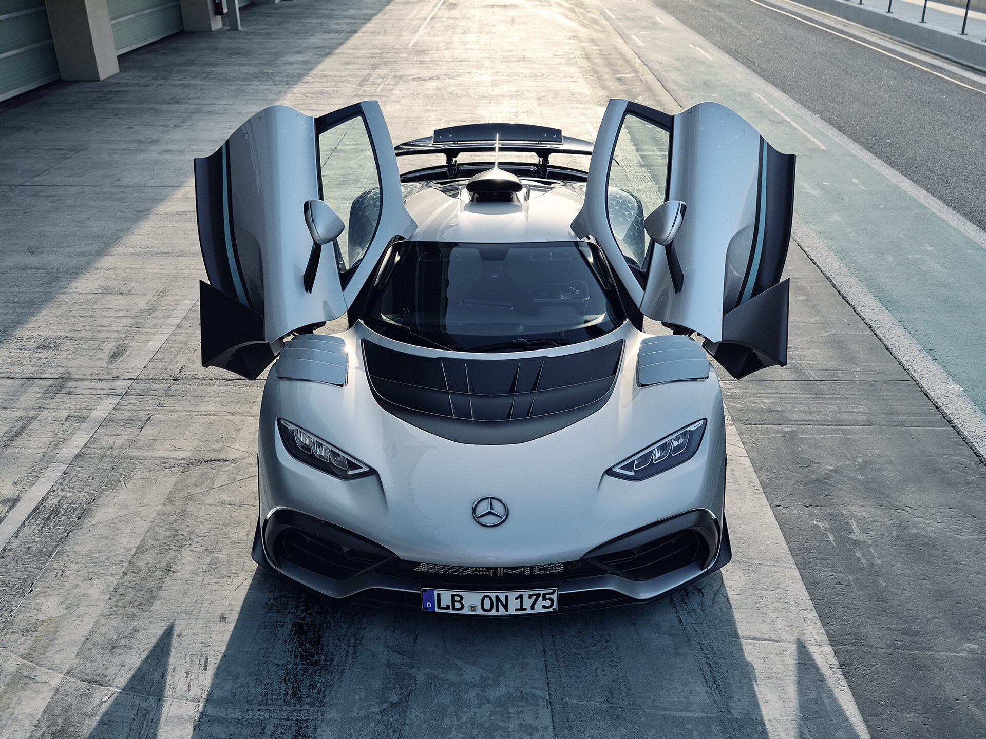 Draufsicht auf ein silbernes Mercedes-AMG ONE Hypercar mit geöffneten Flügeltüren auf einer Rennstrecke.