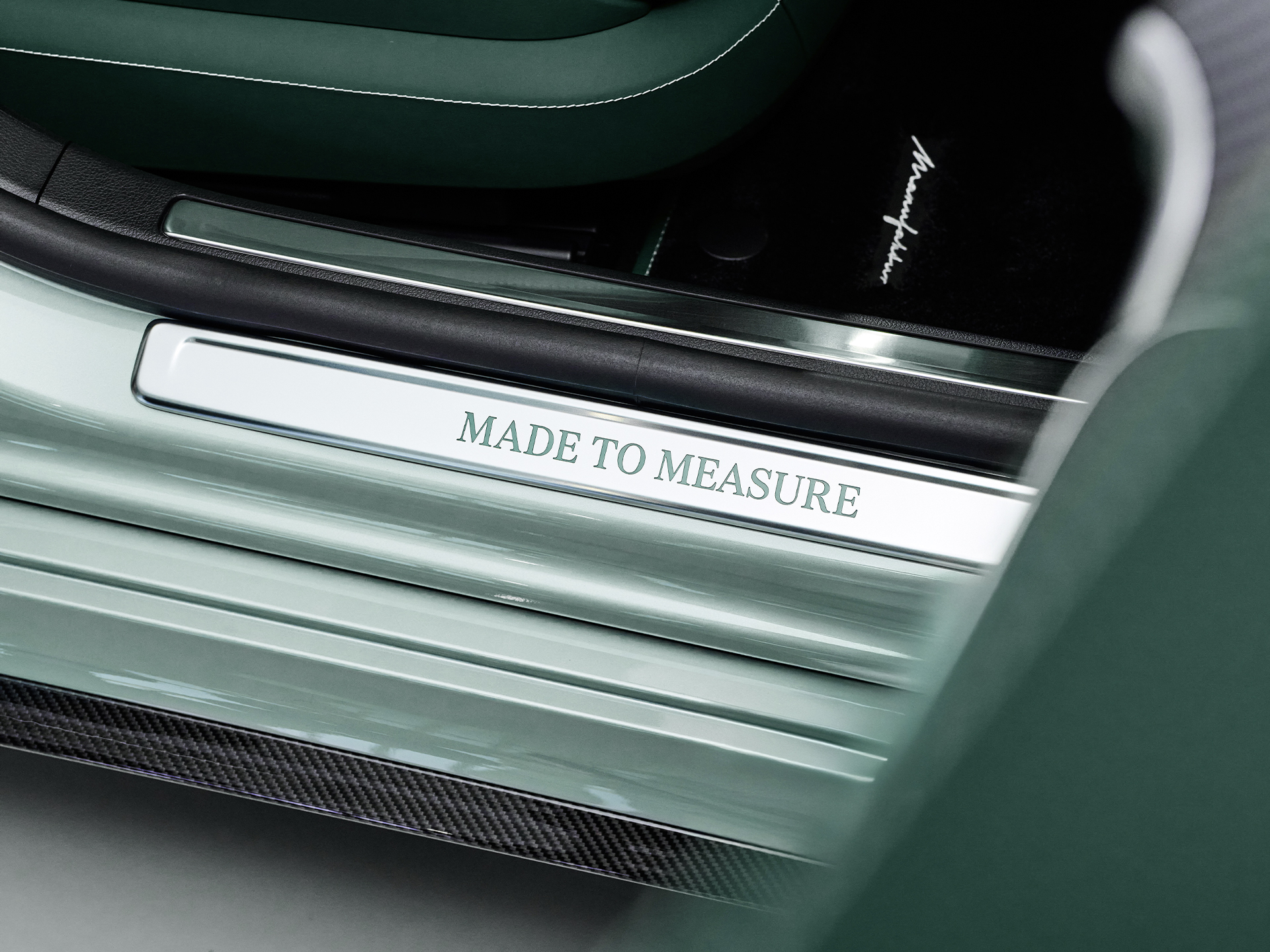 MANUFAKTUR | Mercedes-AMG Eine Einstieglsiete mir "Made to Measure"-Schriftzug an einem grünen Fahrzeug.
