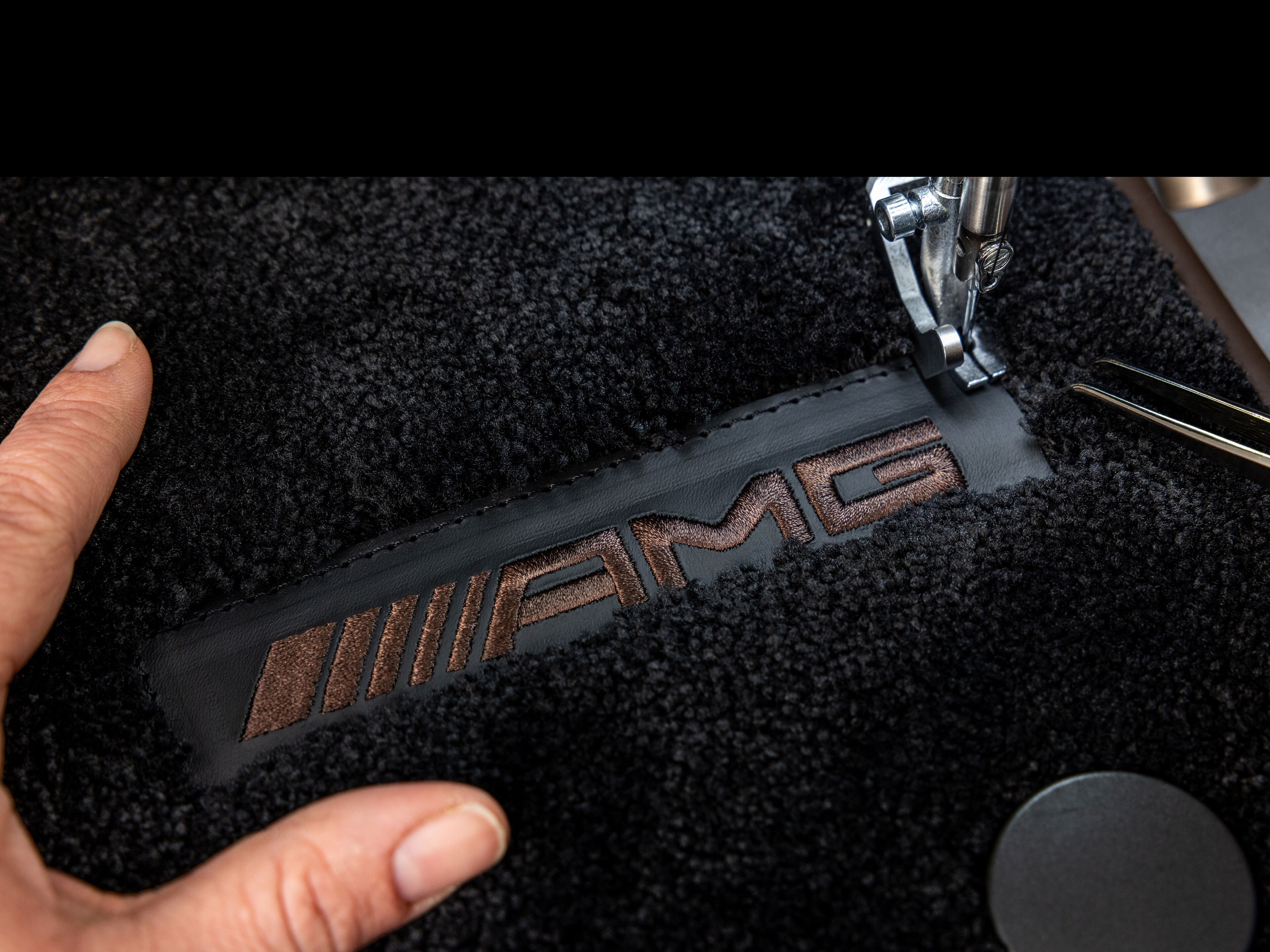 Eine schwarze Fußmatte wird in der MANUFAKTUR mit dem Mercedes-AMG Logo bestickt.