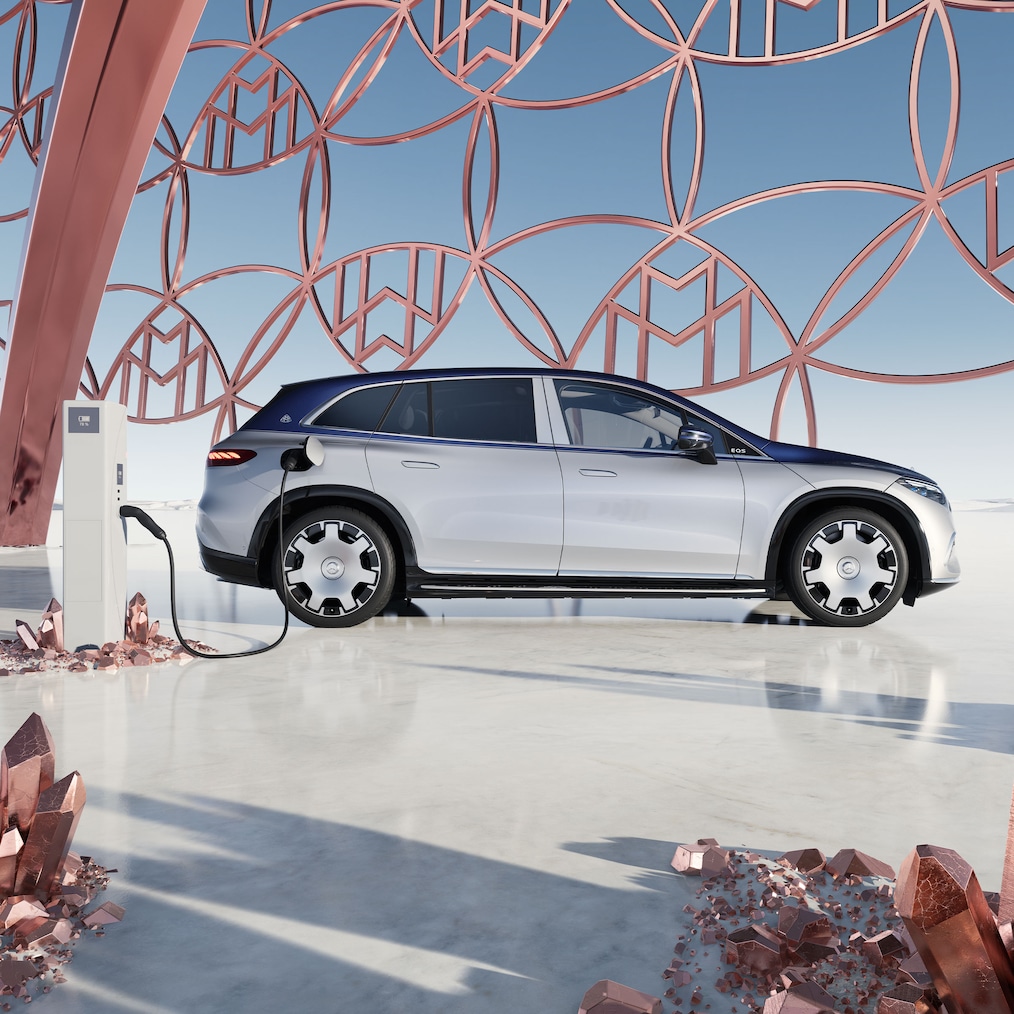 Seitenansicht des Mercedes-Maybach EQS SUV an der Ladestation, mit dem Maybach Markenlogo im Hintergrund.