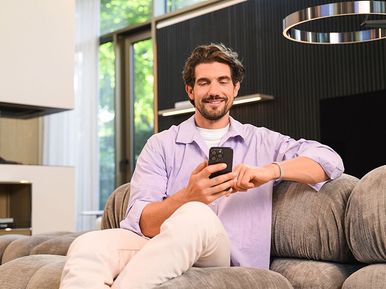 Eine Person sitzt mit einem Handy auf der Couch. 