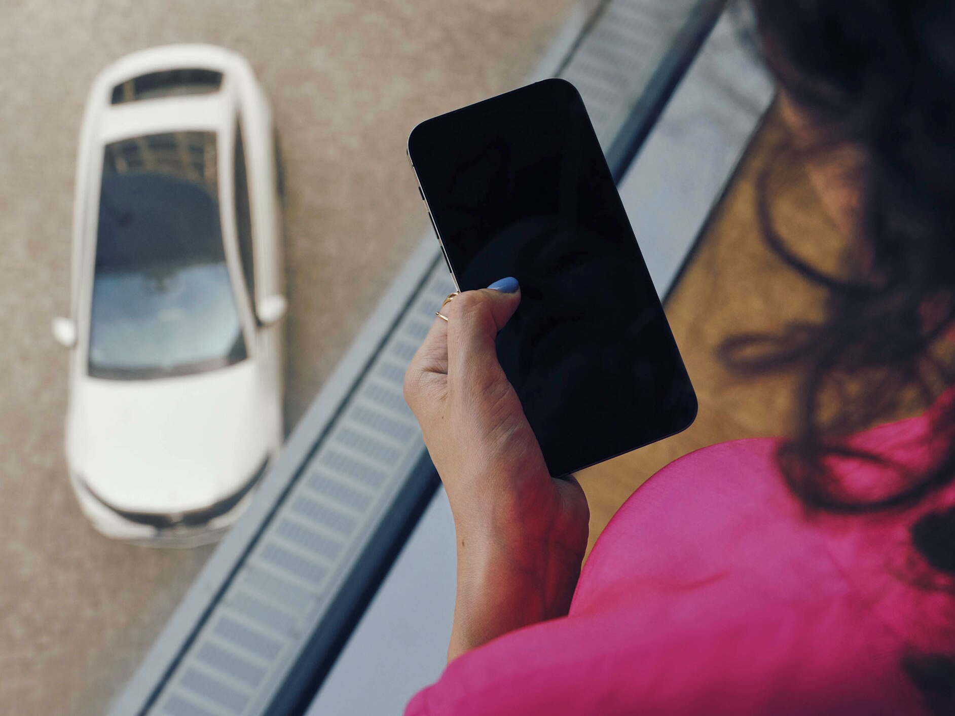 Frau in pink am Handy über einem weißen Mercedes