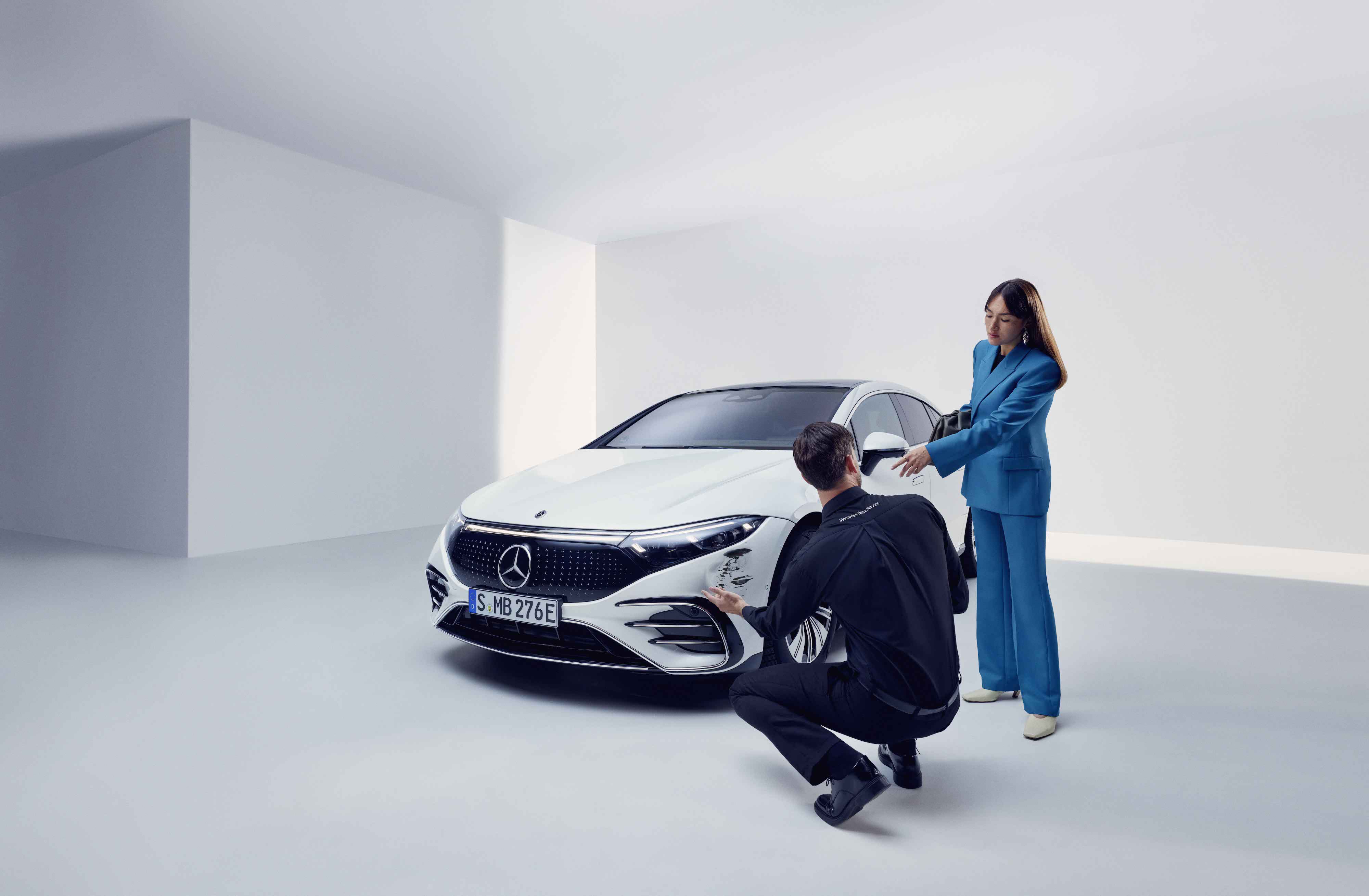 Schadenhilfe | Mercedes-Benz Ein Mann kniet vor einem Auto mit einem Schaden, eine Frau steht daneben.