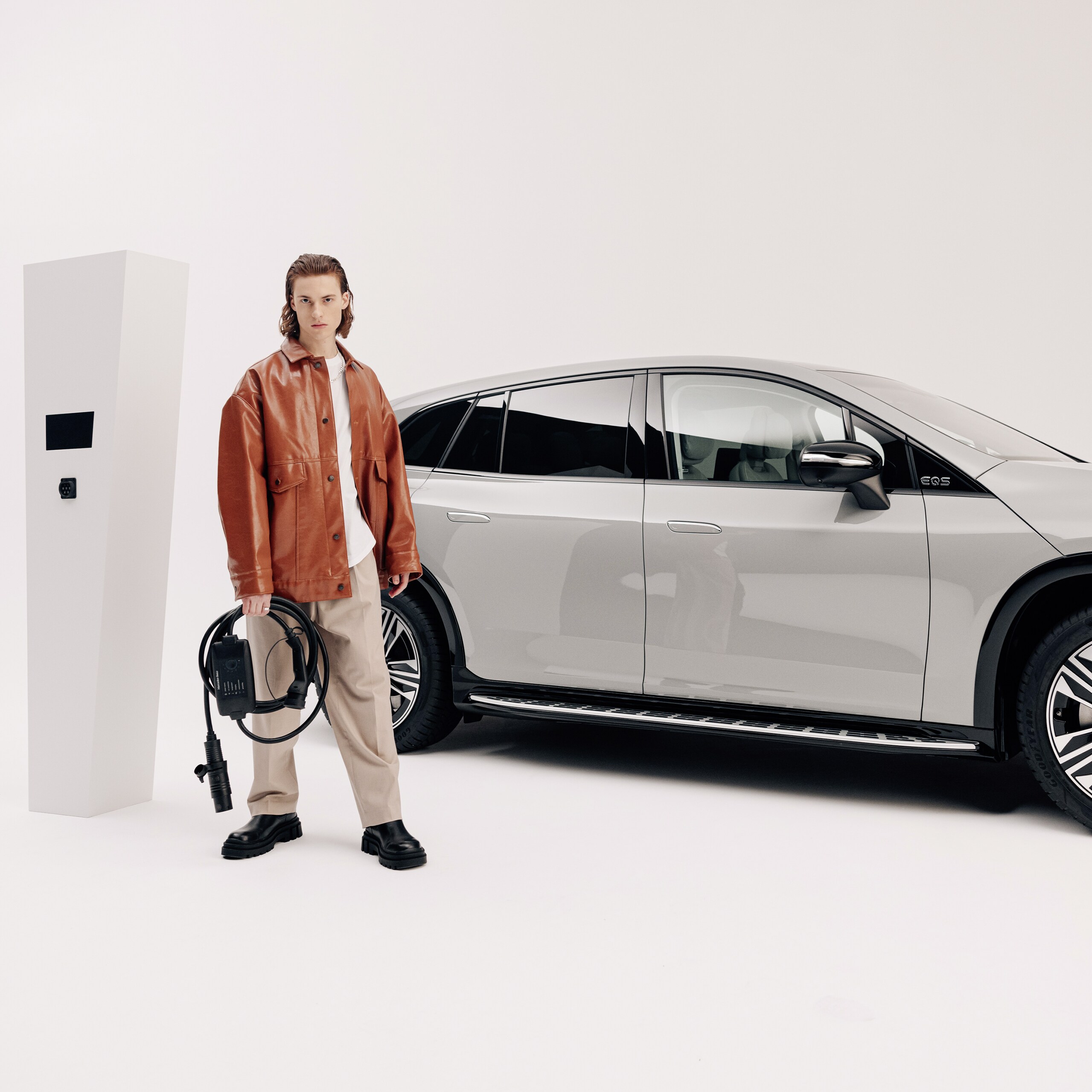 Ein junger Mann sthet mit einem Ladekabel vor einem parkendem Mercedes-Benz.