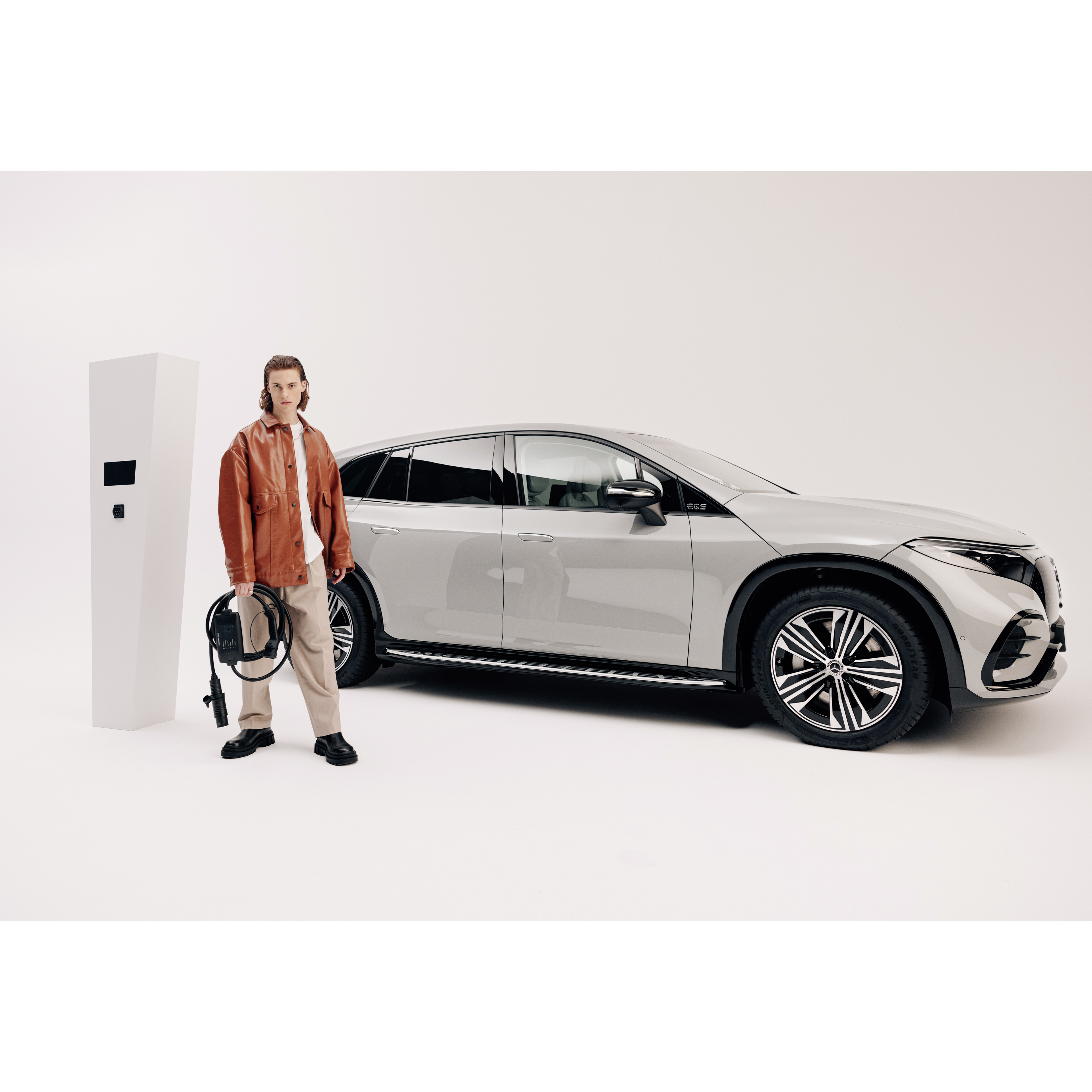 Flexibles Ladesystem Pro | Zu Huase Laden | Mercedes-Benz. Ein junger Mann sthet mit einem Ladekabel vor einem parkendem Mercedes-Benz.