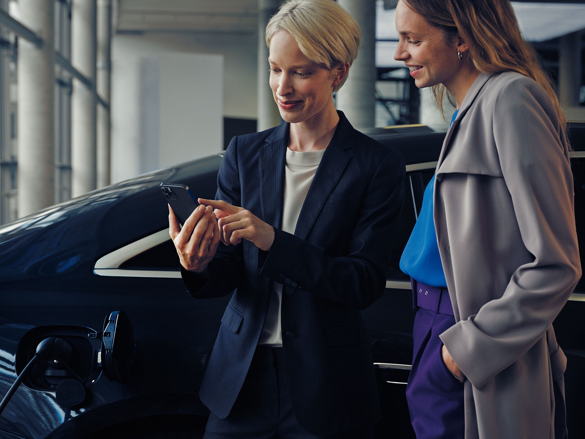 Zwei Frauen vor einer schwarzen Mercedes-Benz EQE-Limousine, die geladen wird.