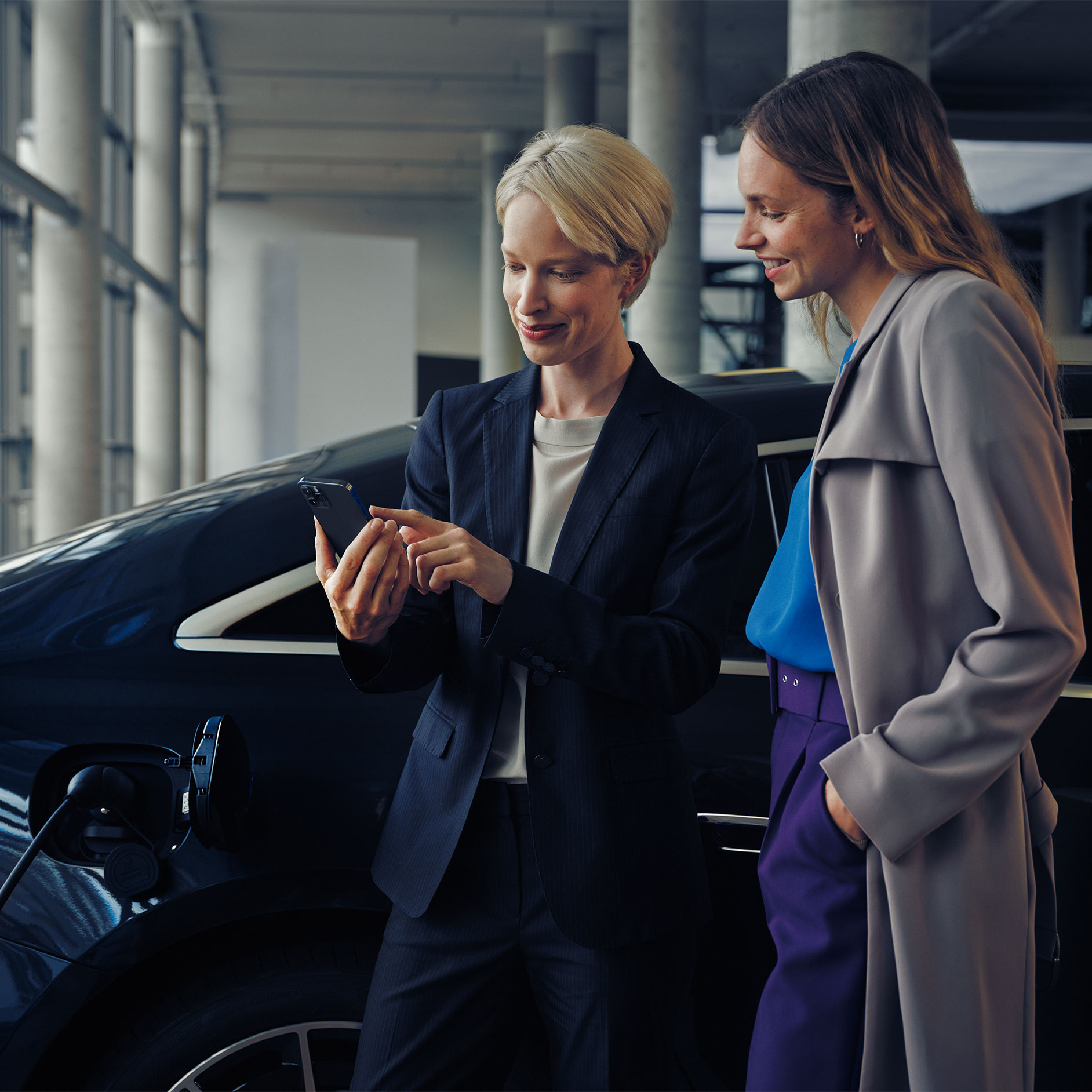 Installationsberatung | Zu Hause Laden | Mercedes-Benz. Zwei Frauen vor einer schwarzen Mercedes-Benz EQE-Limousine, die geladen wird.