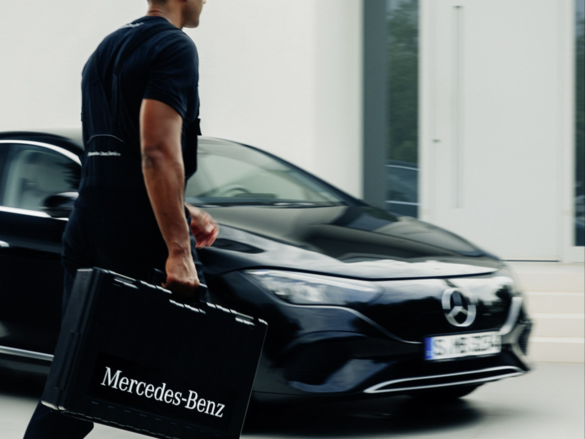 Ein Mann mit einem schwarzen Koffer vor einem elektrischen Mercedes-Benz Fahrzeug.