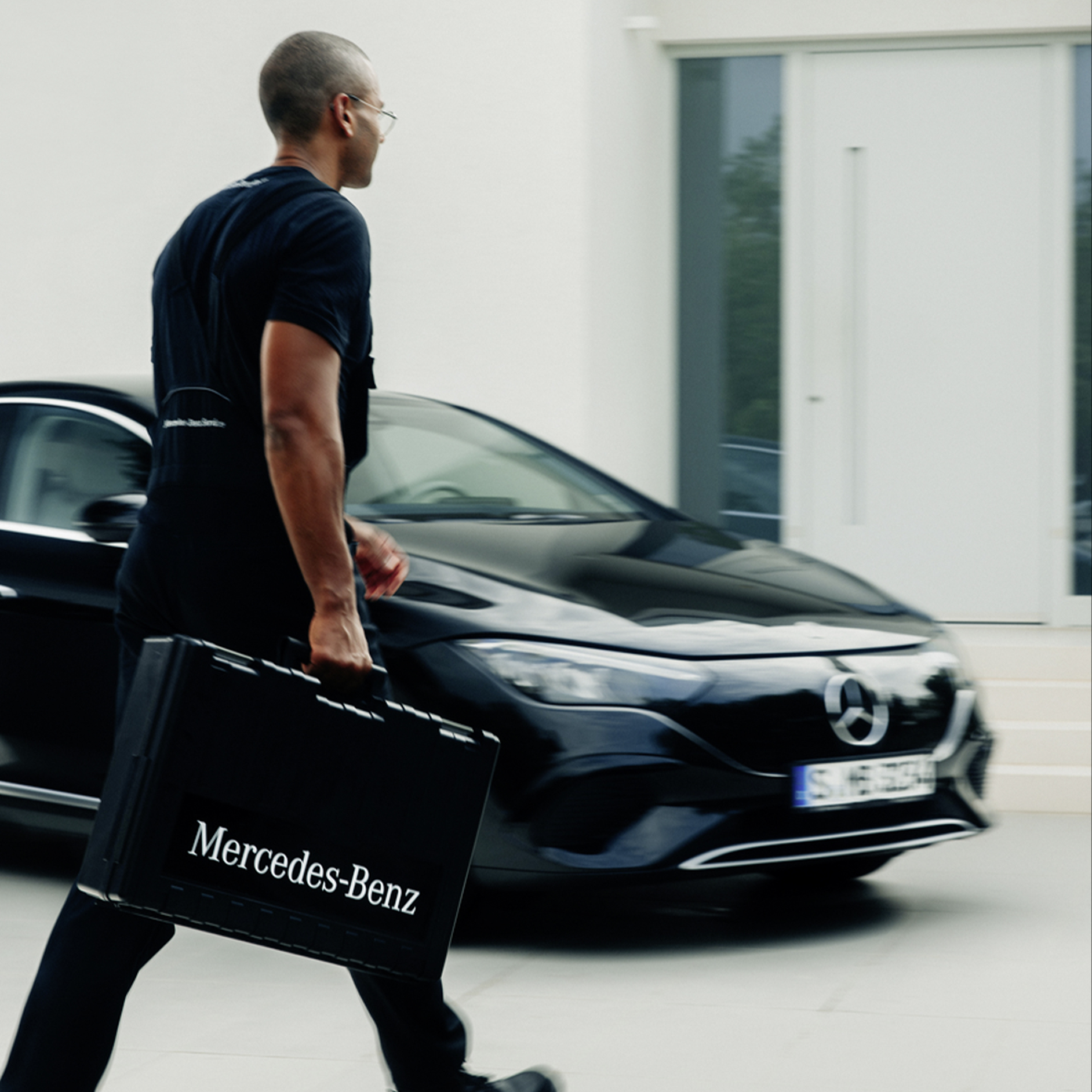 Installation | Zu Hause Laden | Mercedes-Benz. Ein Mann mit einem schwarzen Koffer vor einem elektrischen Mercedes-Benz Fahrzeug.