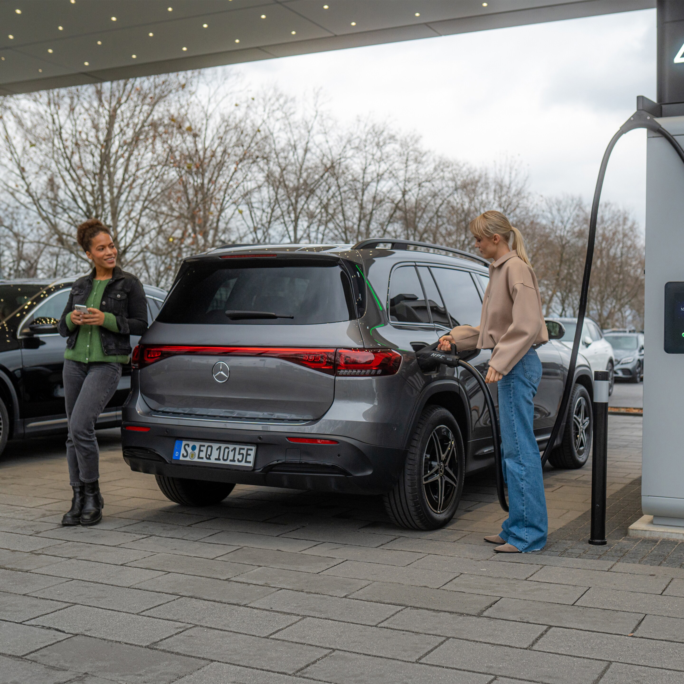Eine junge Frau betankt Ihr Mercedes-Benz Elektroauto an einer Mercedes-Benz Ladestation.